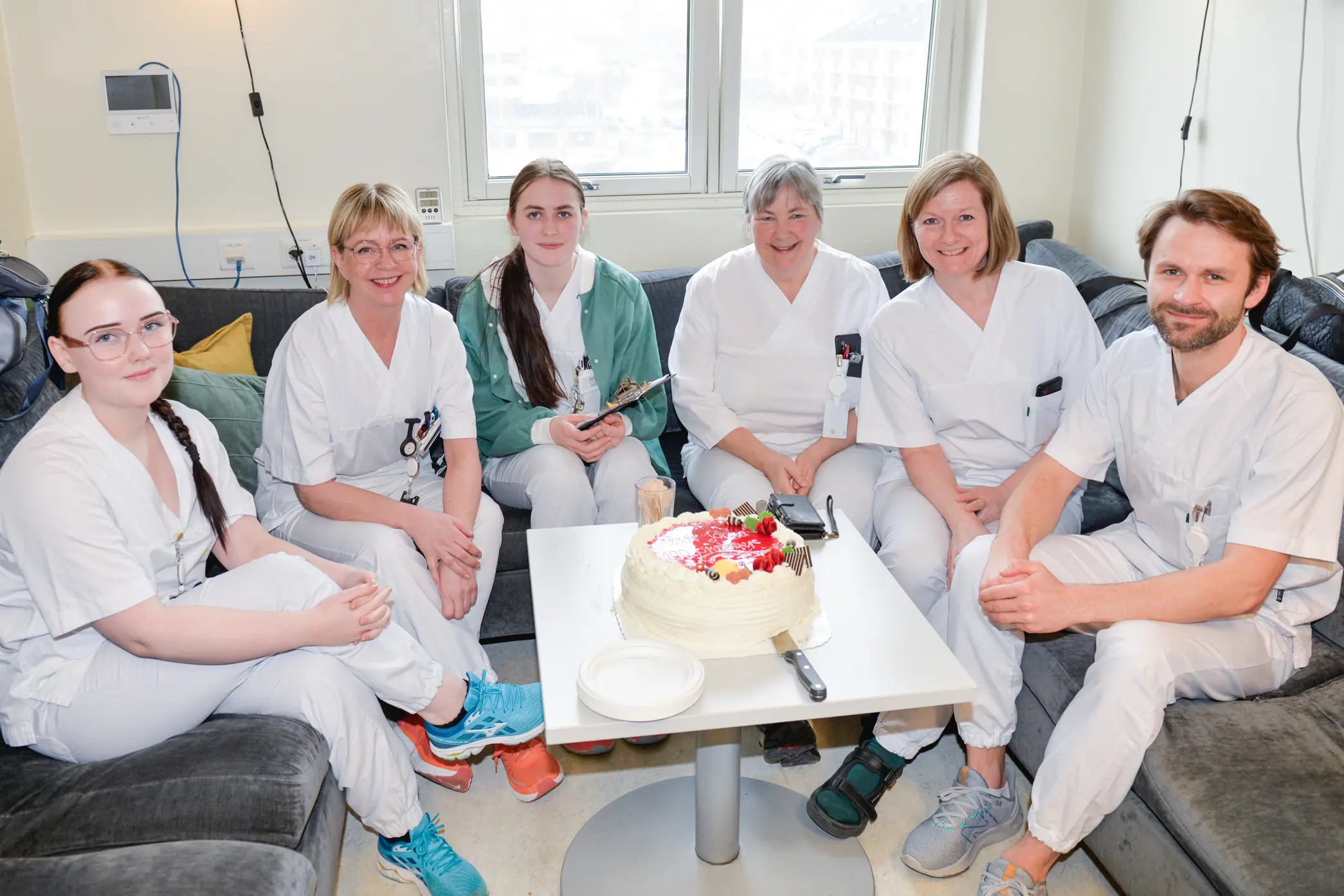 Seks hvitkledte mennesker sitter rundt et bord med kake