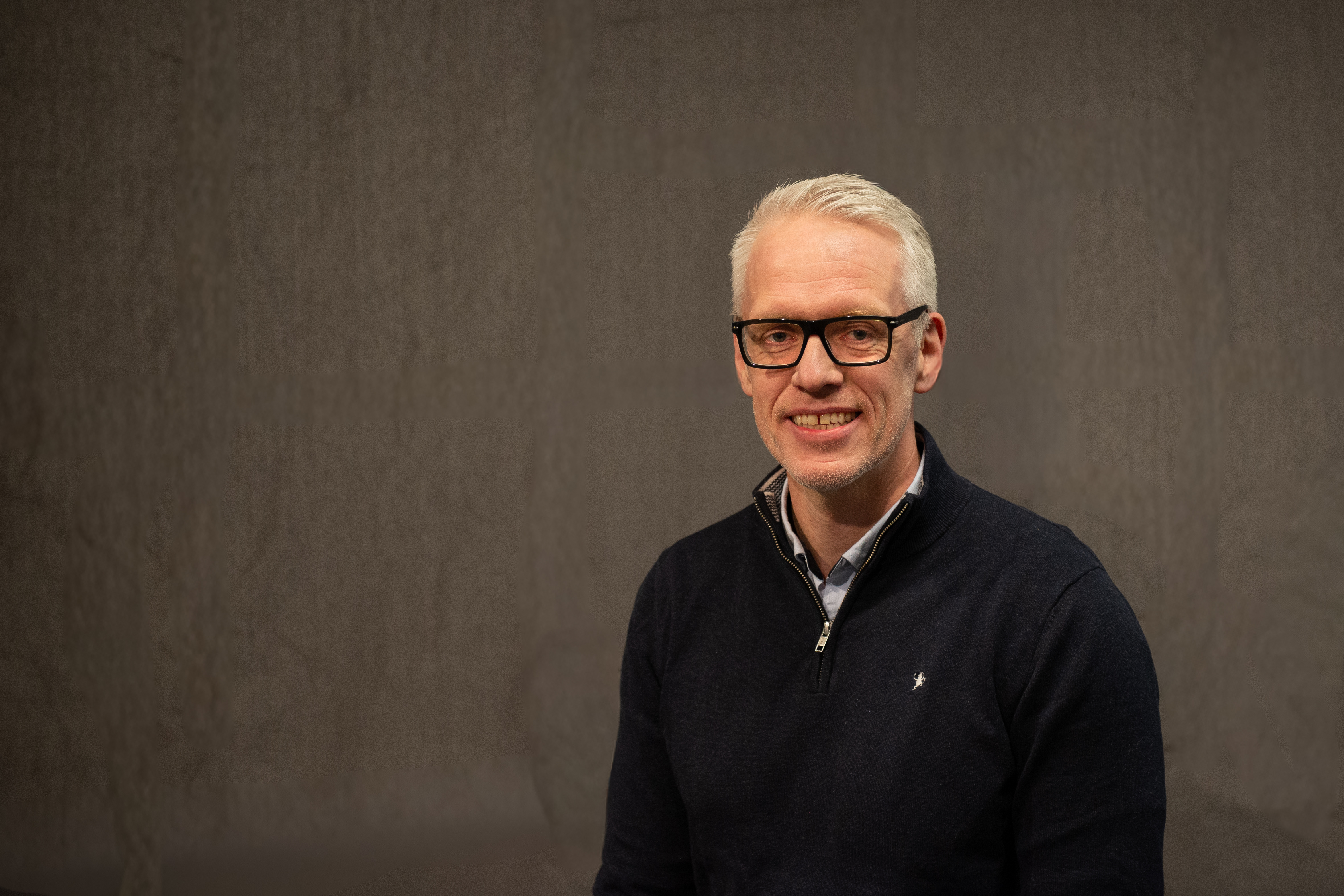 Mann med svarte briller smiler mot kamera