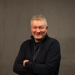 Mann med armene i kors, smiler mot kamera