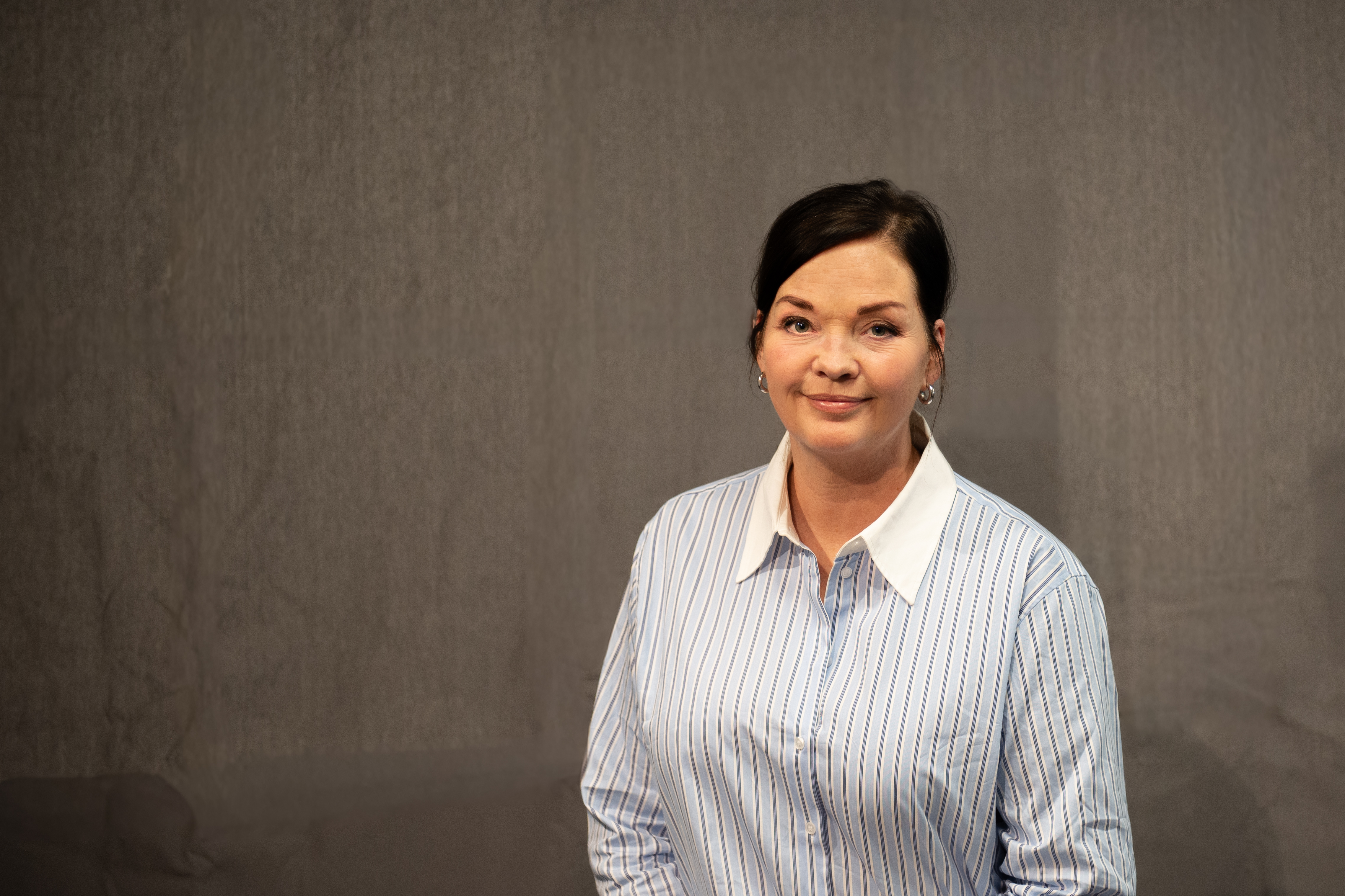 Dame med mørkt hår i hestehale poserer for et portrett mens hun ser inn i kamera