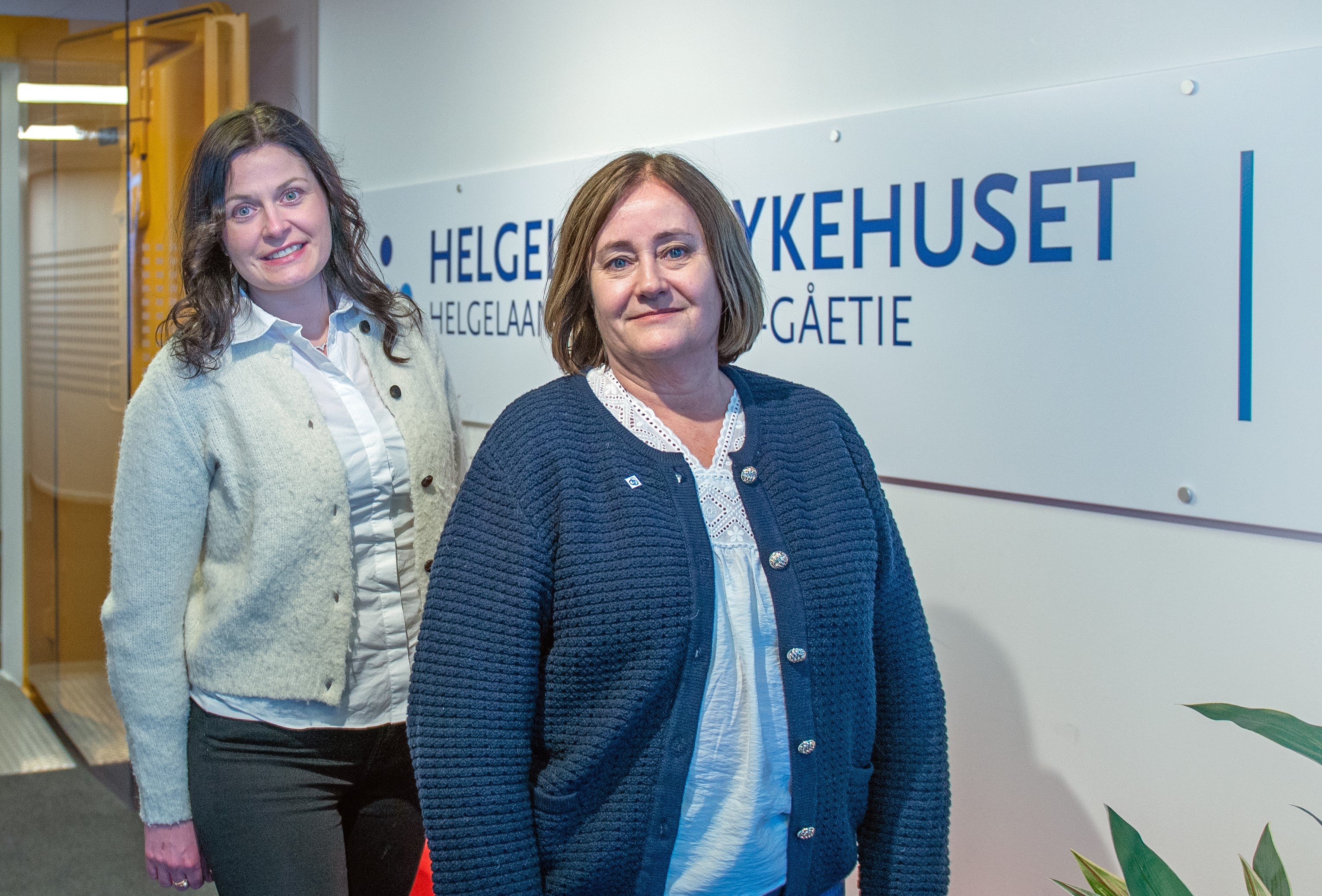 Et par kvinner som står foran et skilt