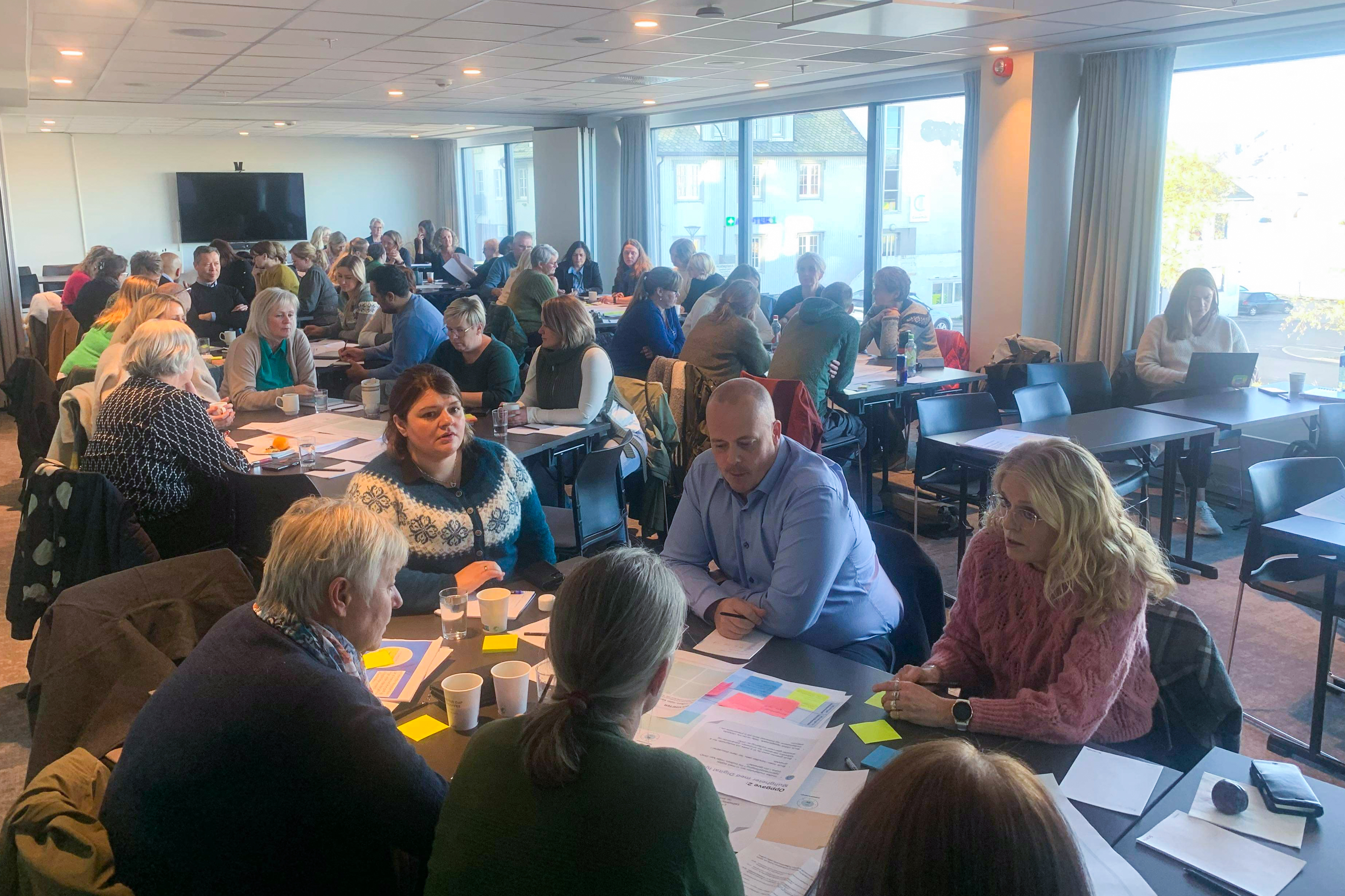 Mange personer sitter tett rundt mange bord i en stor sal