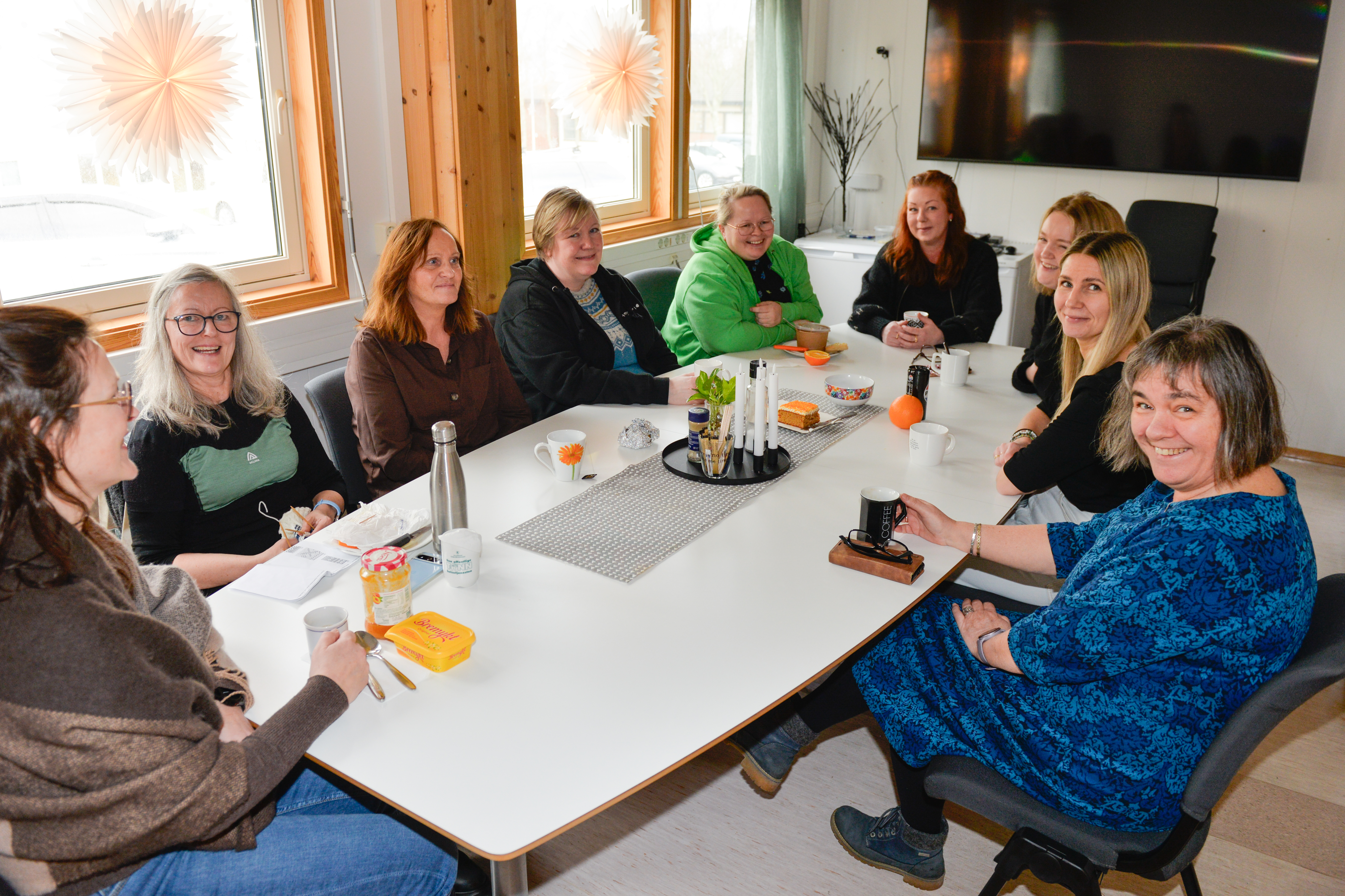 En gruppe mennesker sitter og spiser og prater rundt et lunsjbord