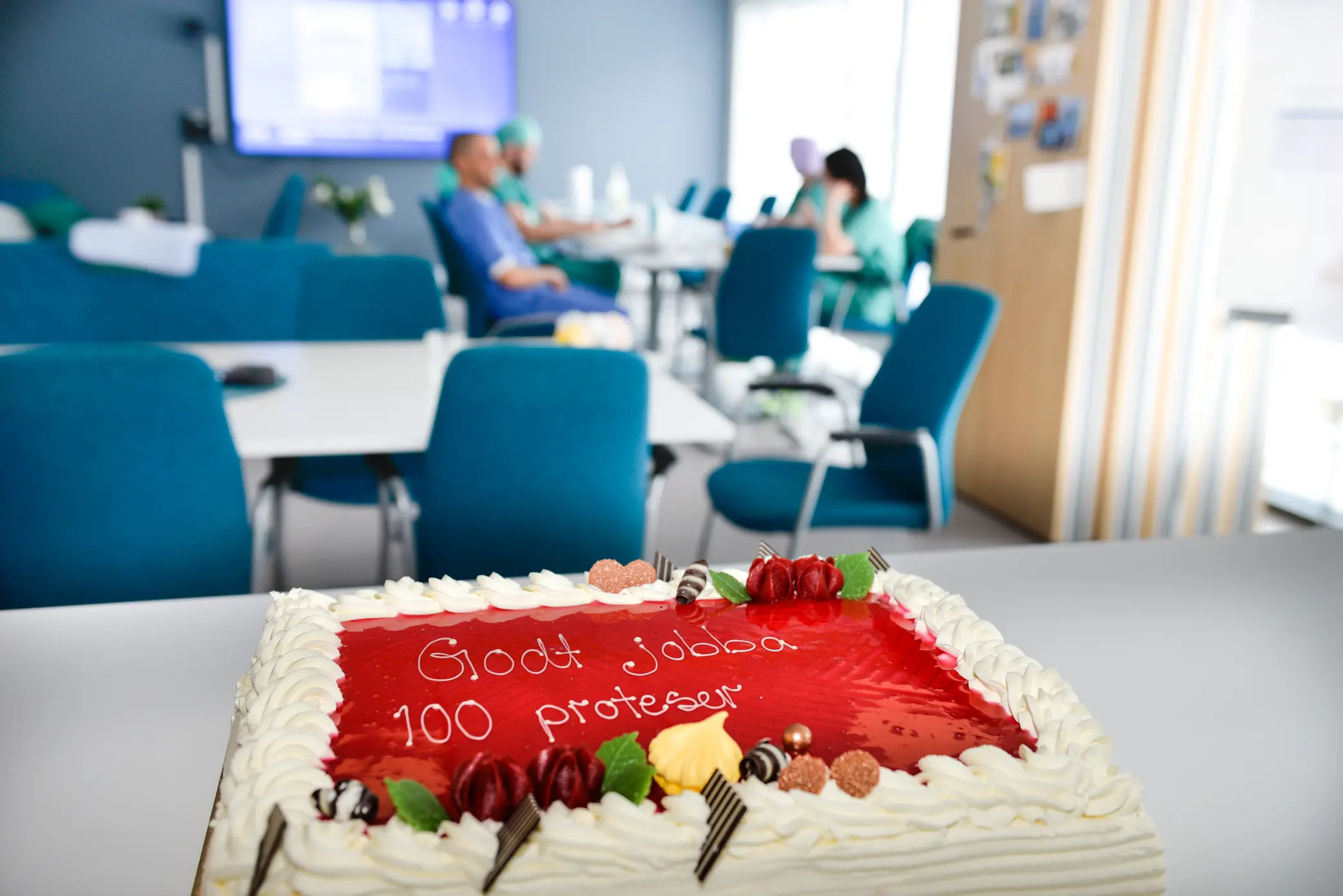 Stor kake på et bord med mange mennesker sittende langt bak