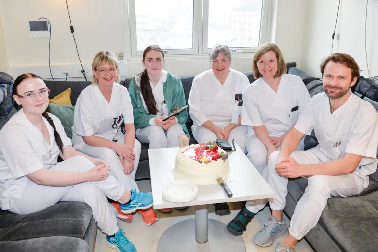 Seks hvitkledte mennesker sitter rundt et bord med kake