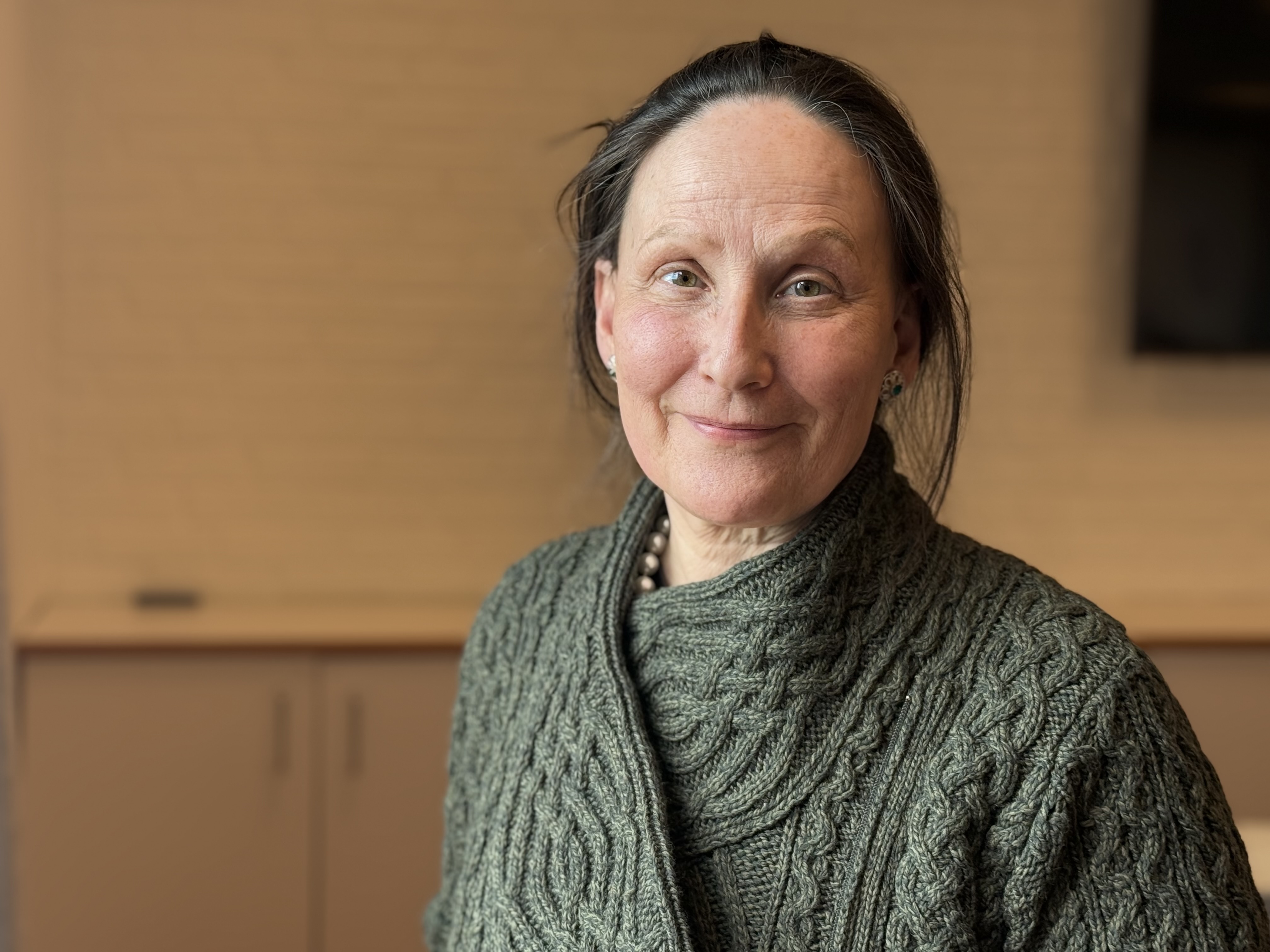 En voksen dame med langt hår som smiler til kameraet