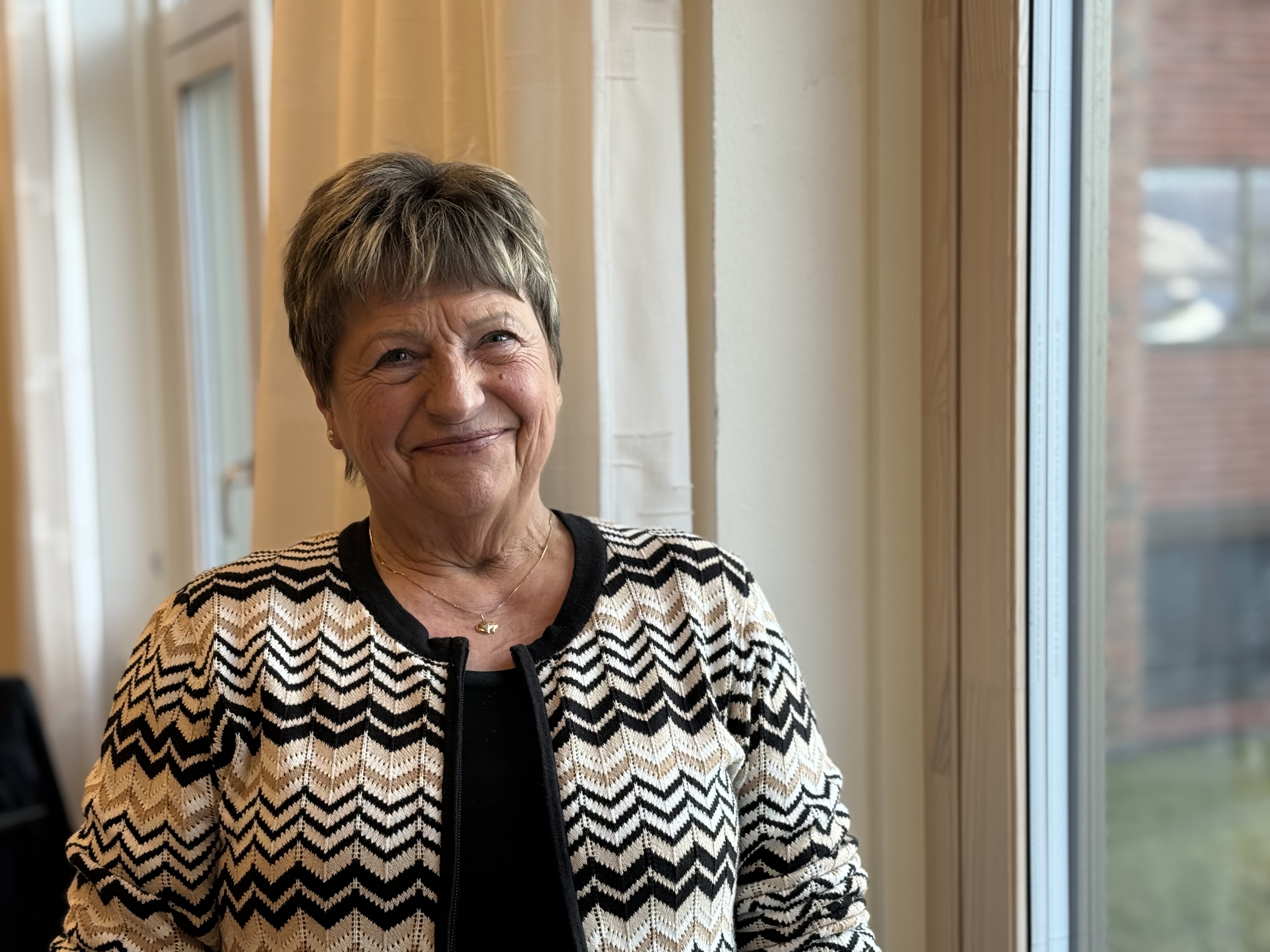 En voksen dame med kort hår som smiler til kamera