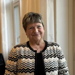 En voksen dame med kort hår som smiler til kamera