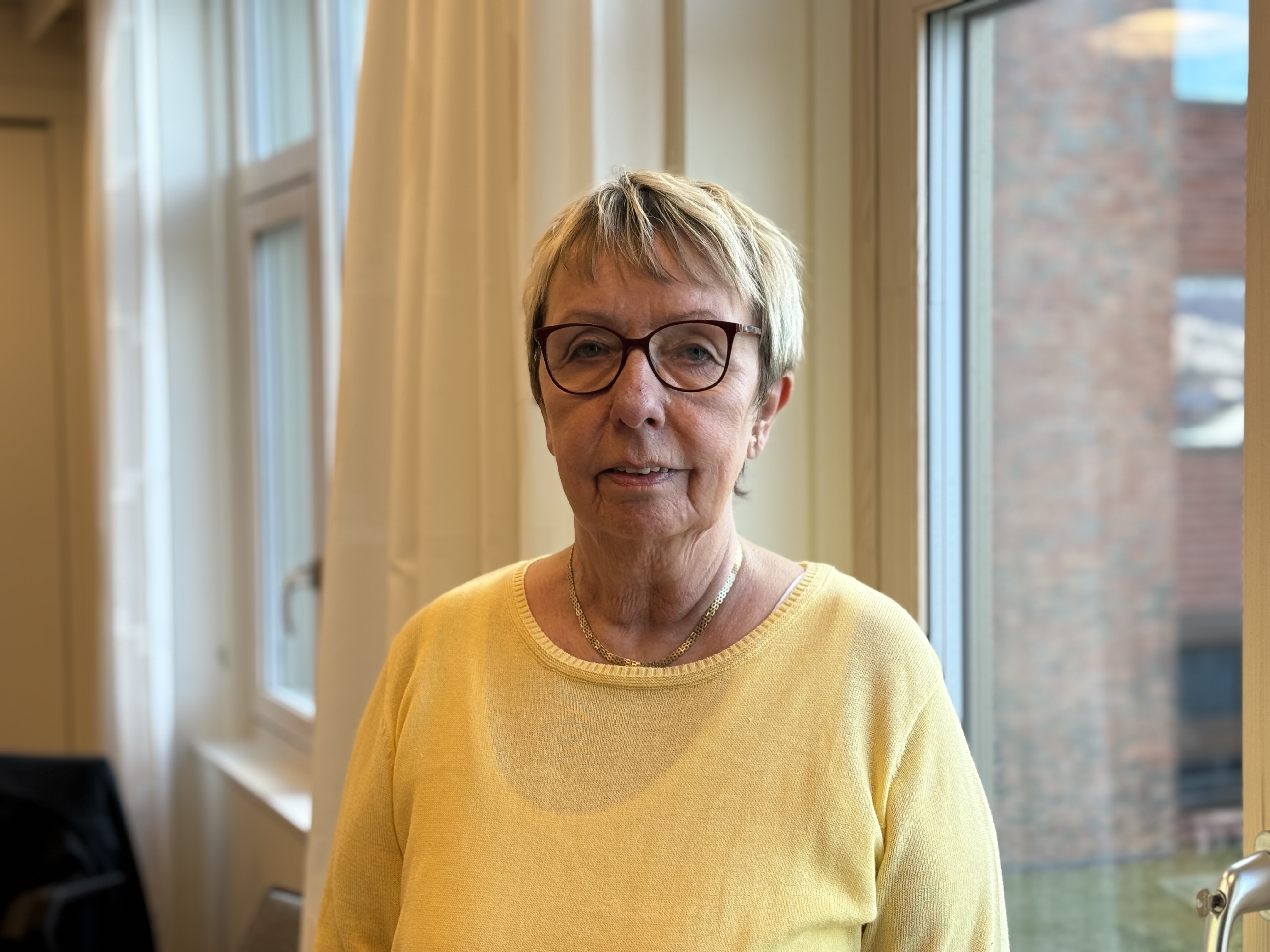 En voksen dame med kort lyst hår og briller ser i kamera