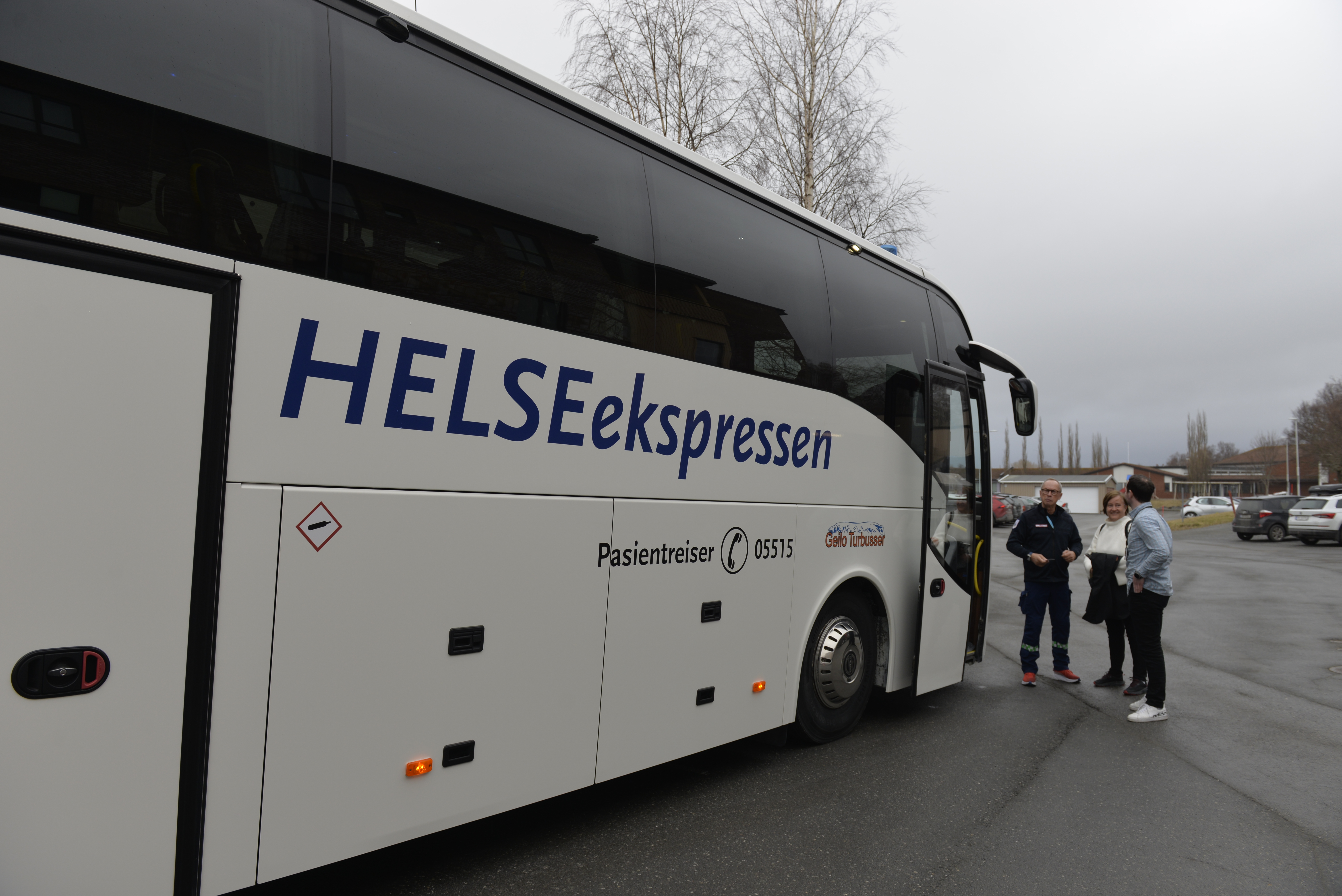 Stor hvit buss med tre personer som står utenfor og prater
