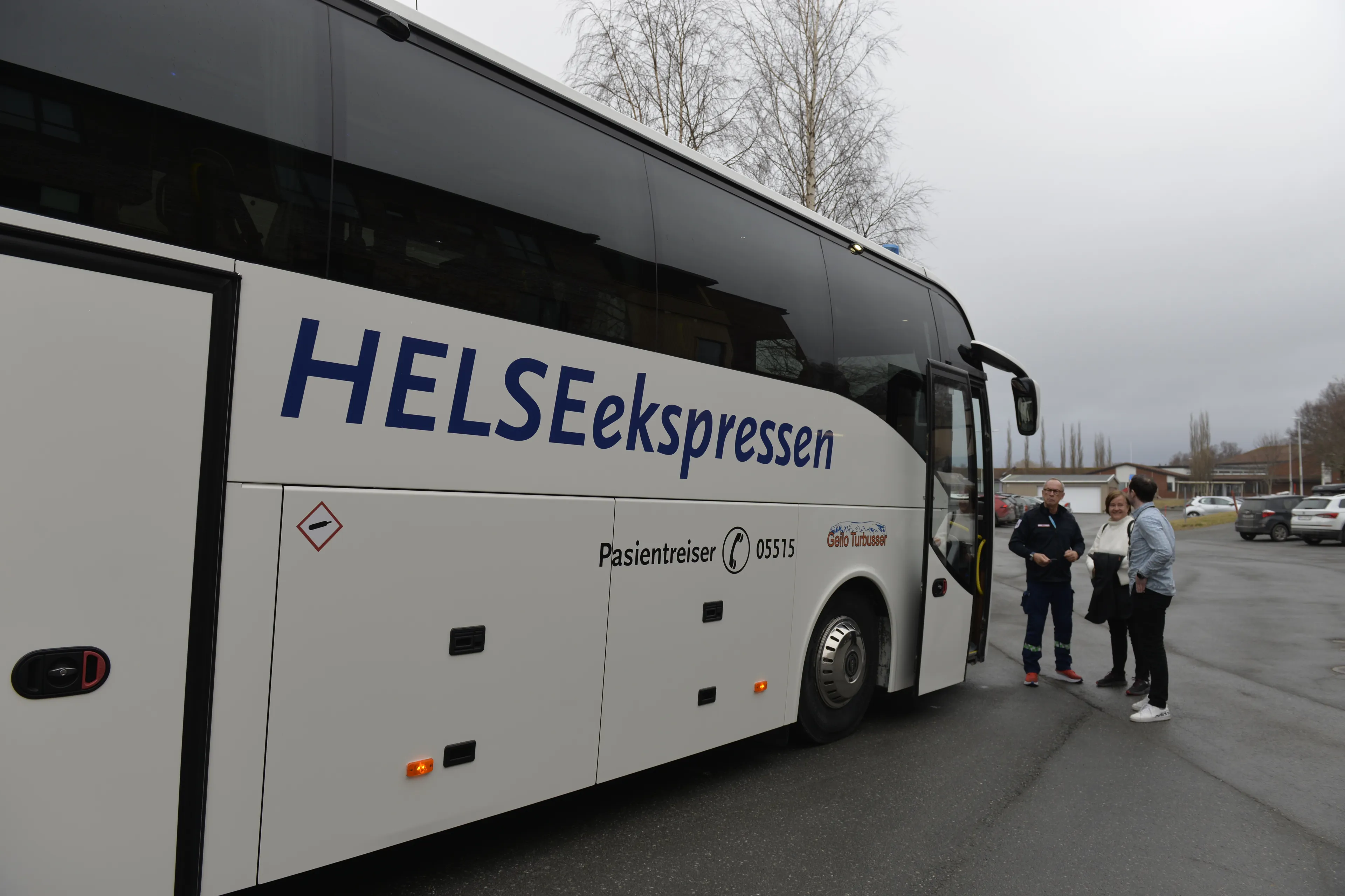Stor hvit buss med tre personer som står utenfor og prater