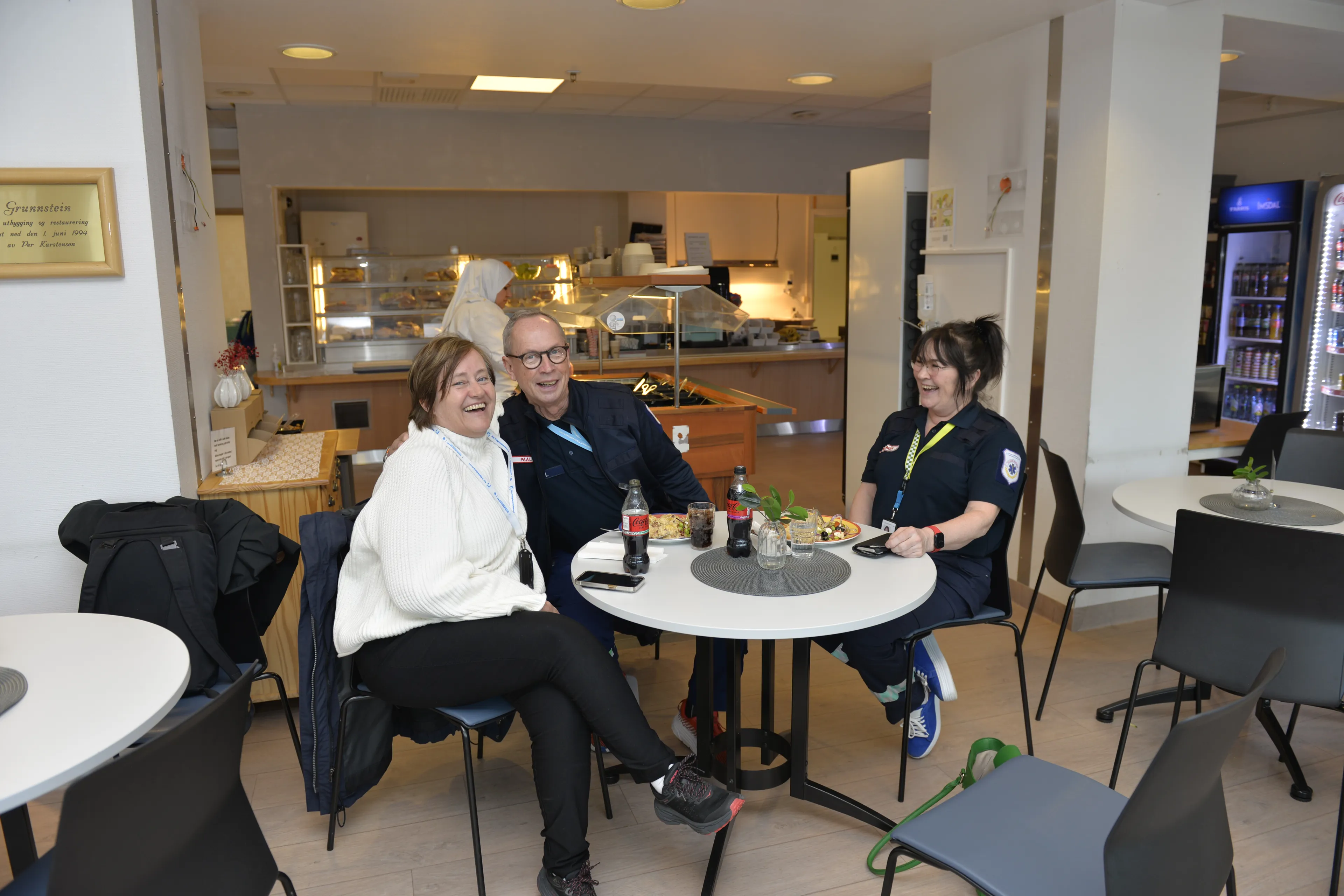 Tre personer spiser lunsj mens de prater og ler