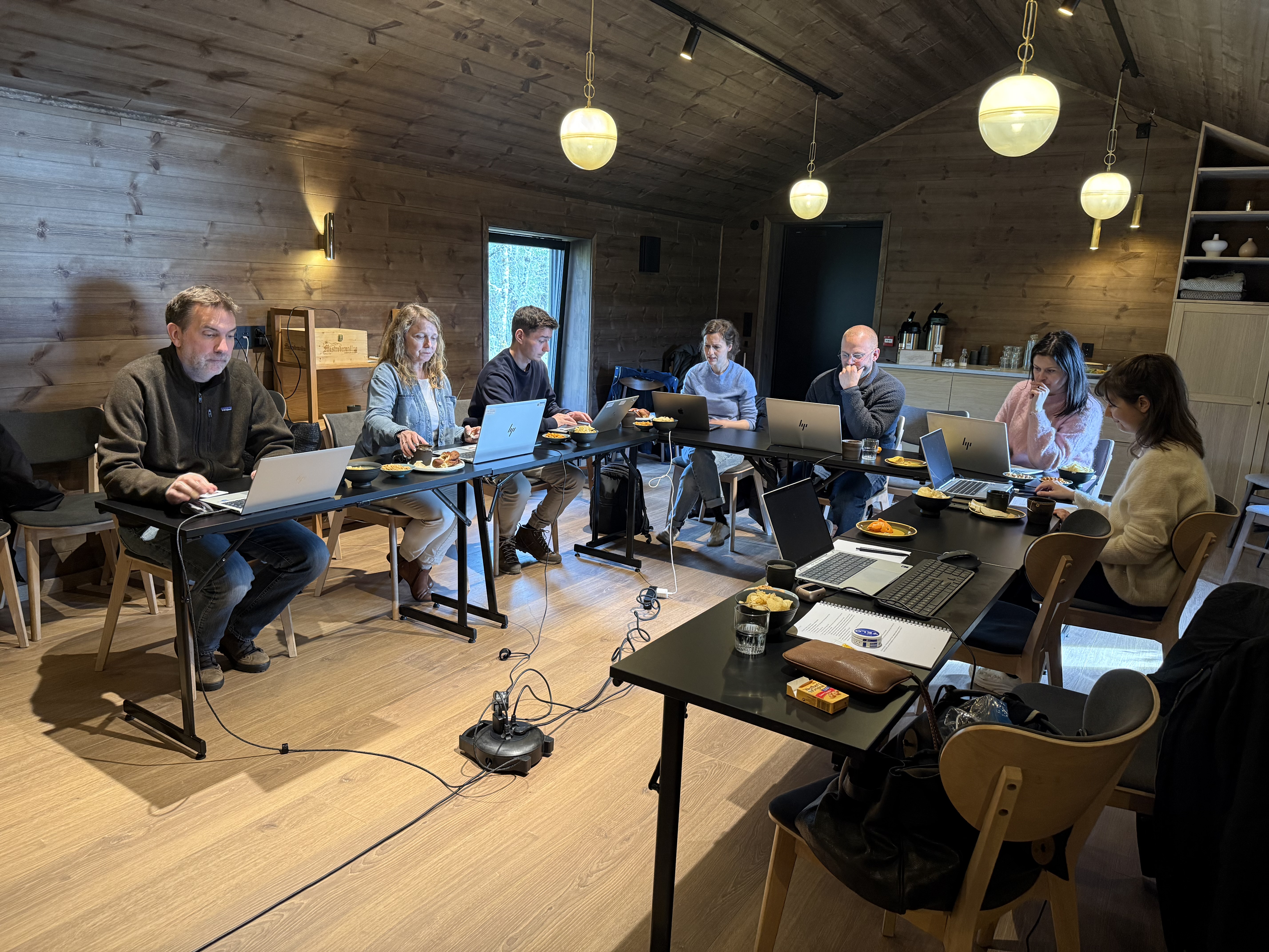 Mange mennesker sitter konsentert med hver sin pc langs et hesteskoformet langbord