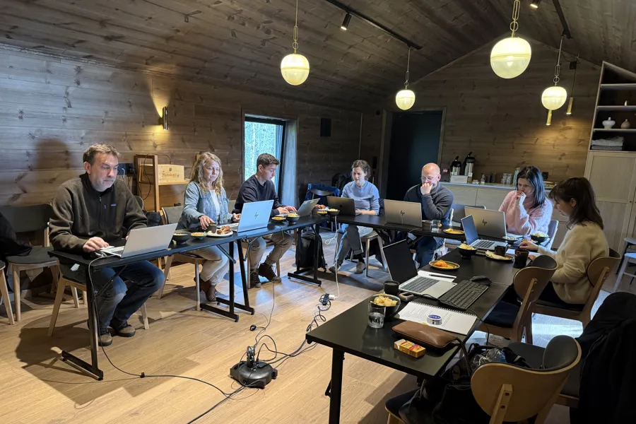 Mange mennesker sitter konsentert med hver sin pc langs et hesteskoformet langbord