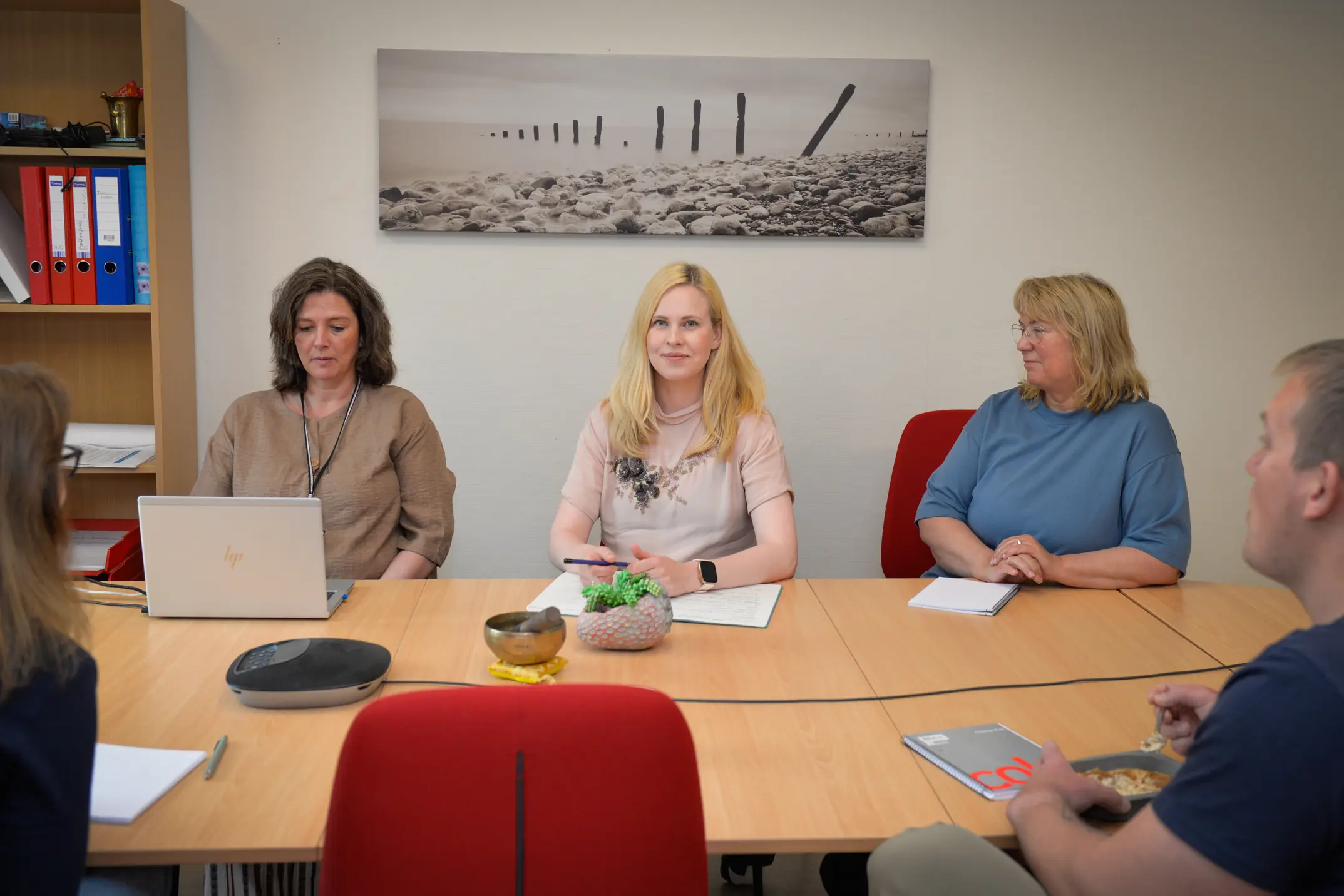 Inne på et møterom sitter fem voksne personer og snakker sammen i forbindelse med et møte