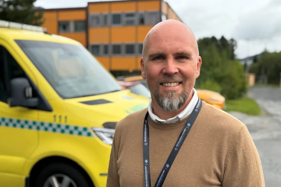 En mann som smiler foran en ambulansebil