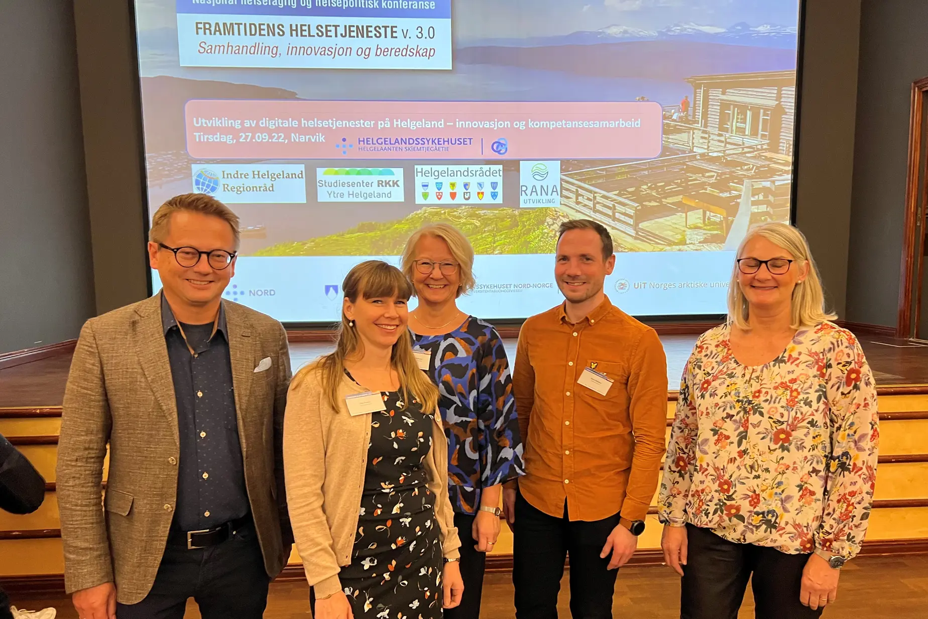 En gruppe mennesker som poserer for et bilde foran en stor skjerm