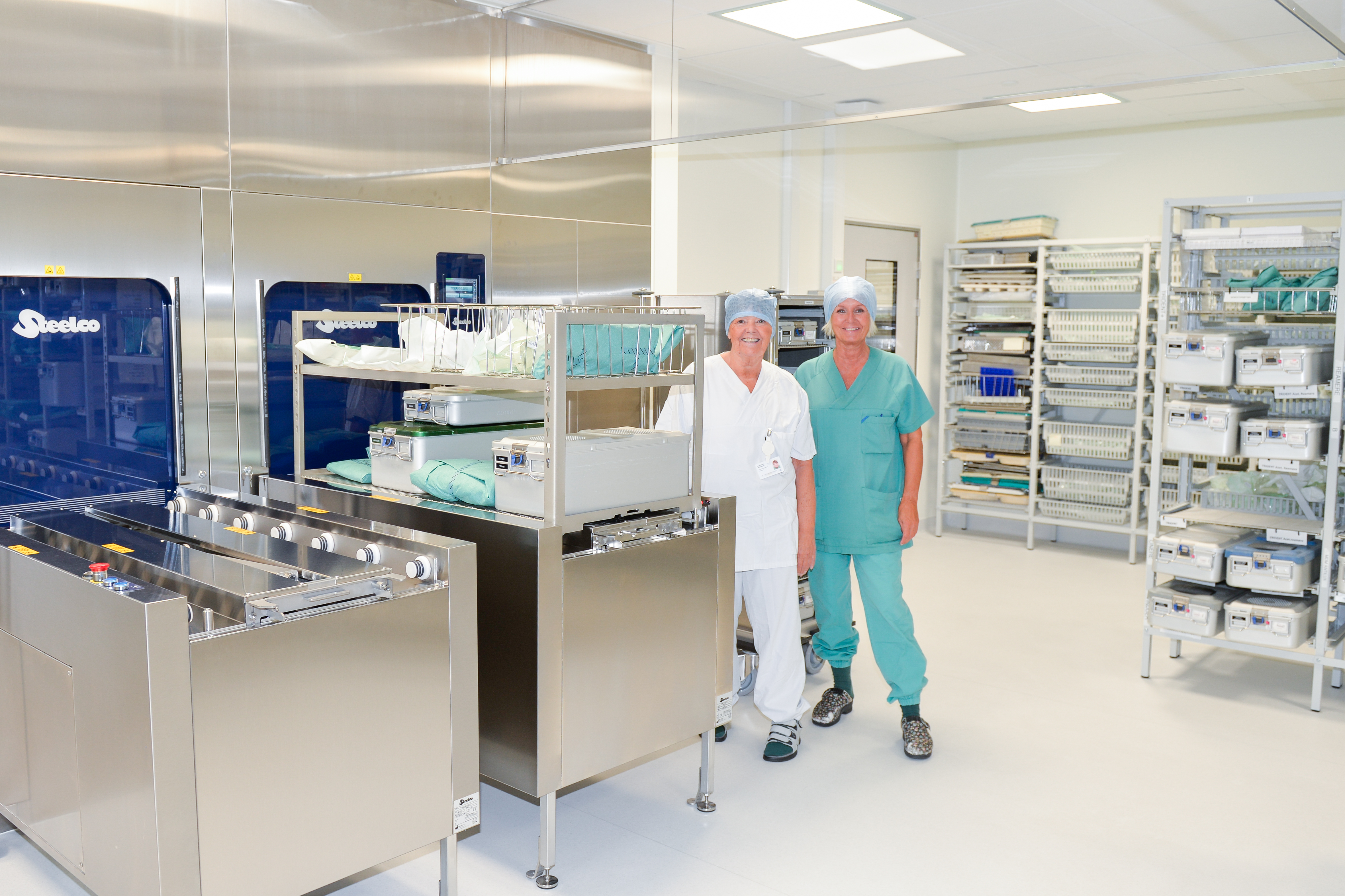 To damer står i Sterilsentralen. Det er mange hyller og bord er.