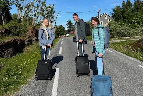 En gruppe mennesker med bagasje som går nedover en vei