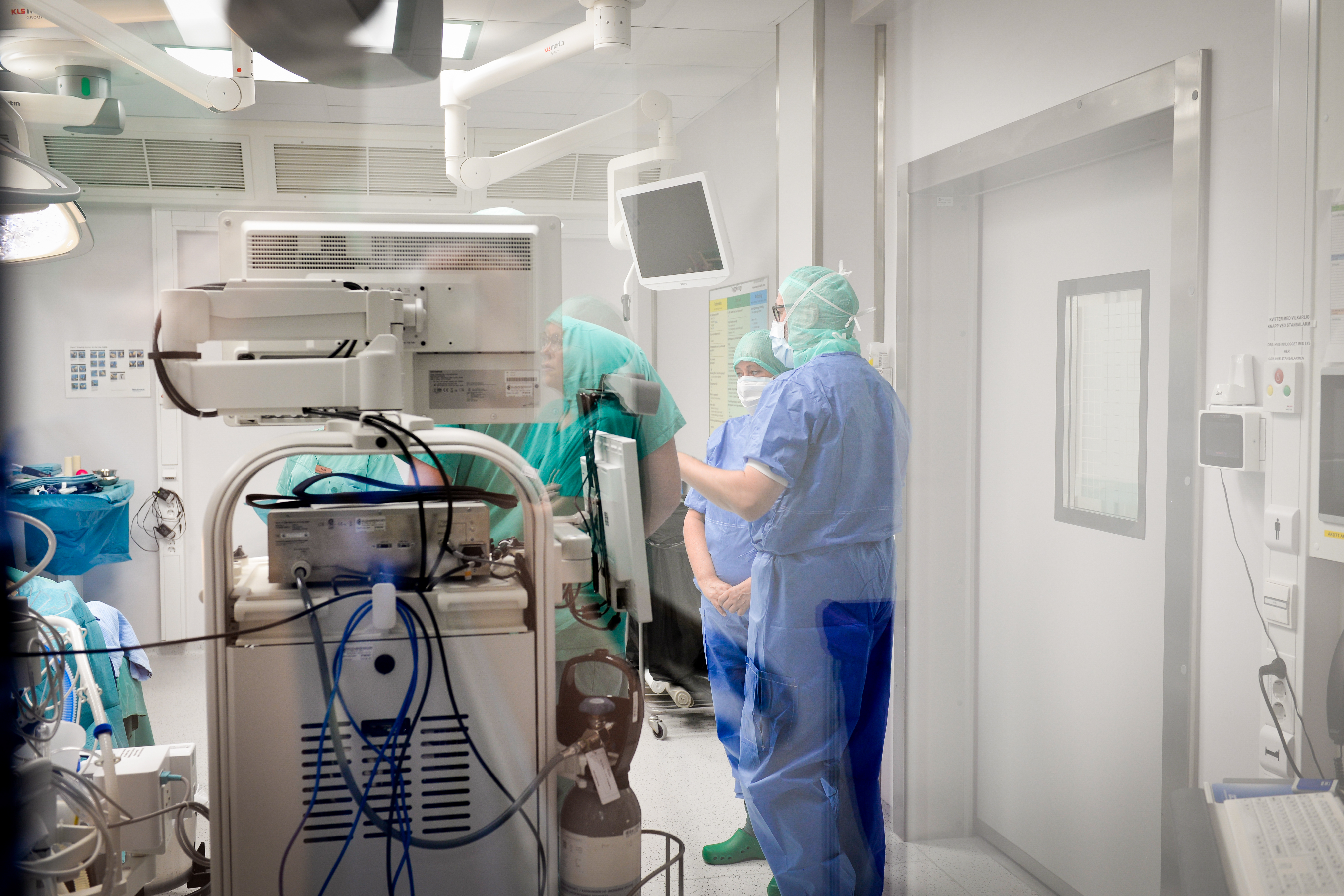 Flere personer i ei operasjonsstue står og prater