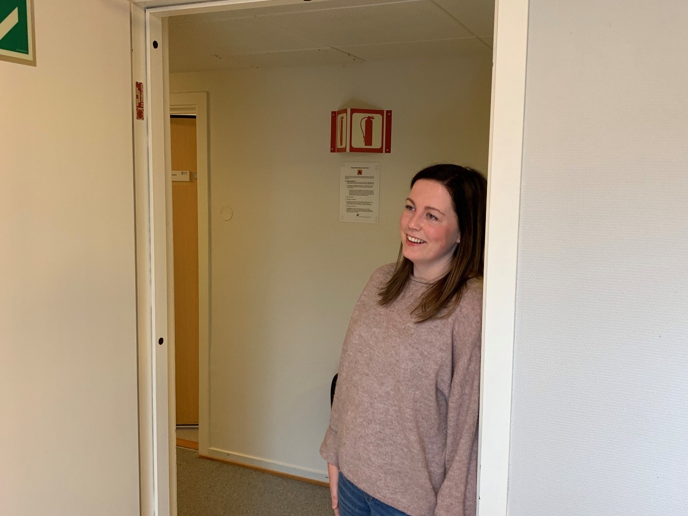 En dame som står i en korridor og lener seg mot en dørkarm
