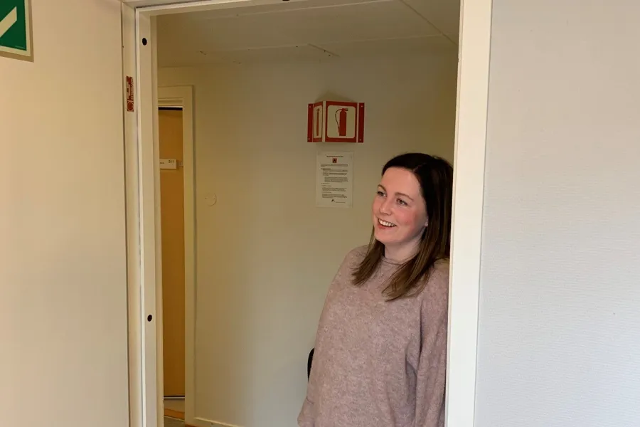 En dame som står i en korridor og lener seg mot en dørkarm