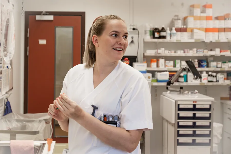 En ung dame i hvit sykepleieuniform snur seg og ser smilende over skulderen