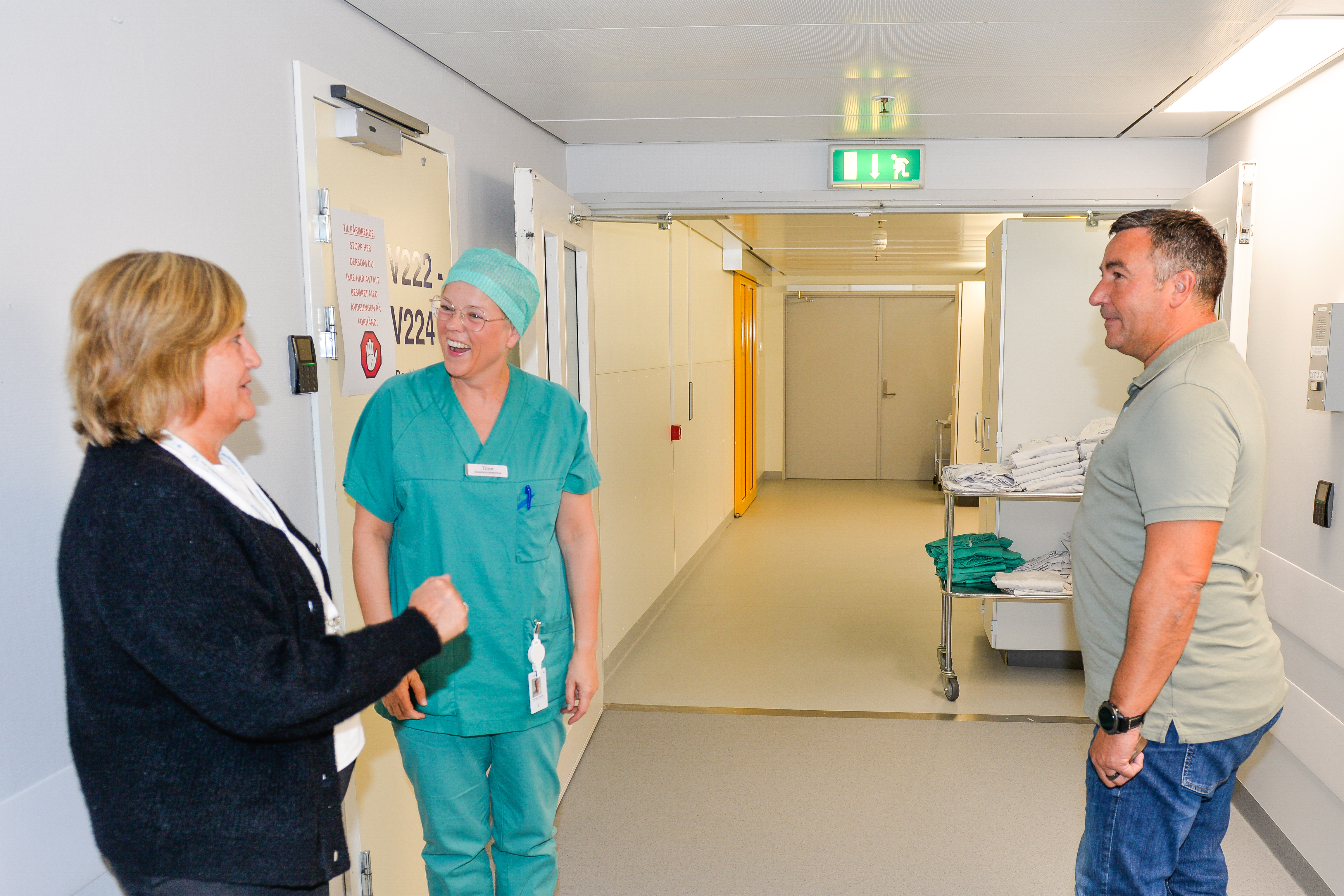 Tre personer prater og ler i en sykehusgang.