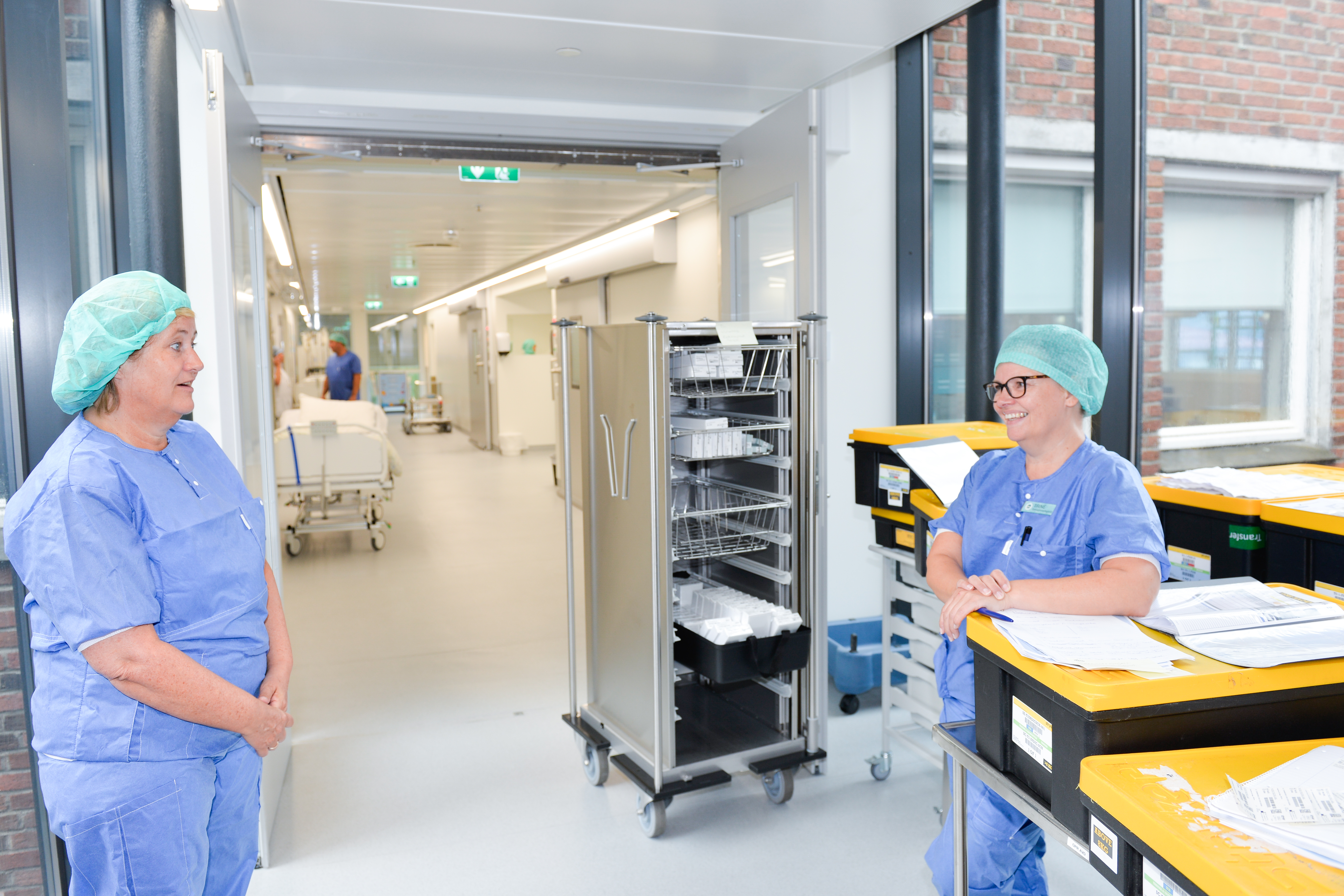 To damer snakker sammen i en gang, de har på sykehusklær