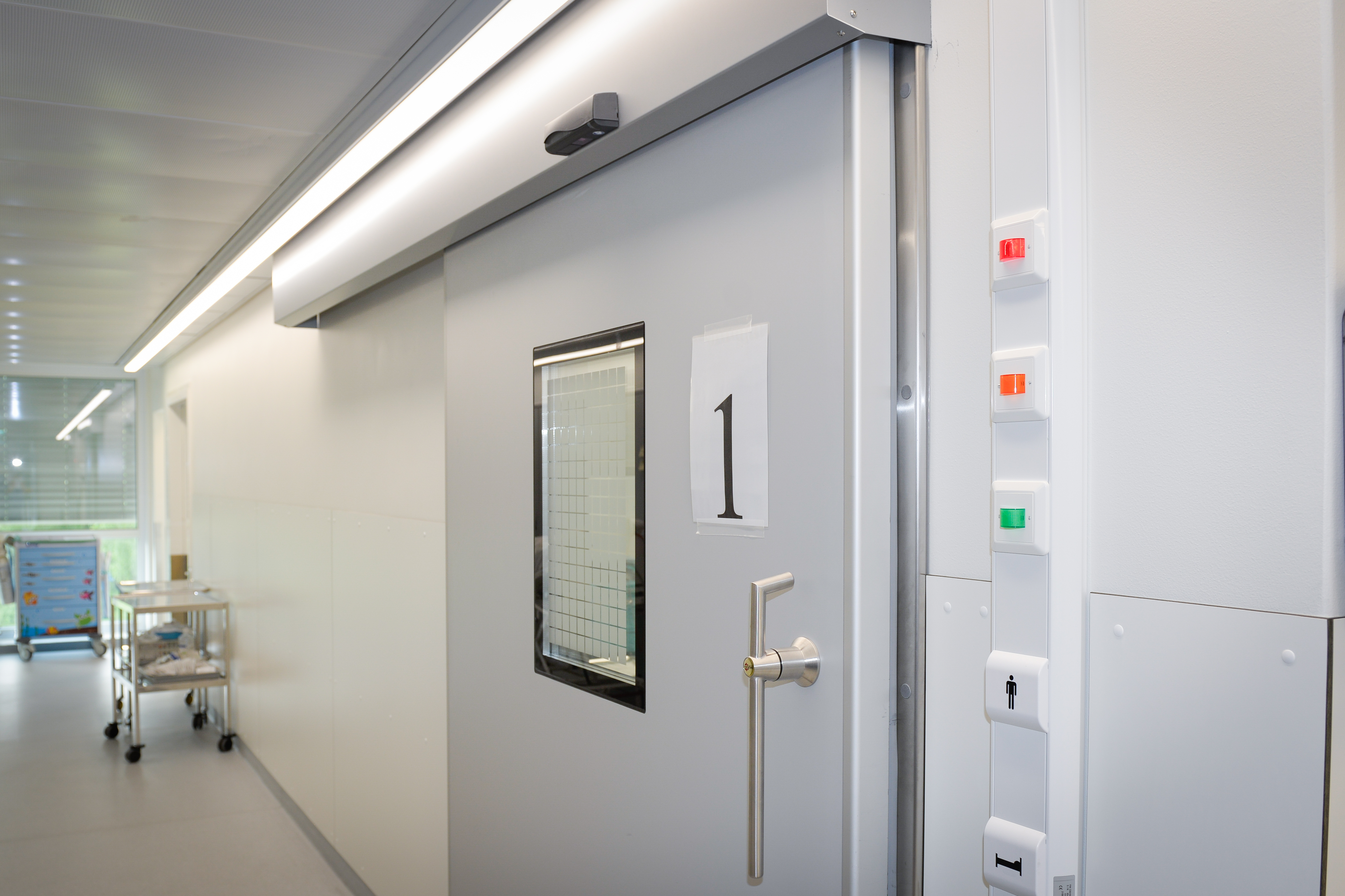 En sykehusgang. Ved ei dør er det ei grønn, en oransje og en rød lampe.