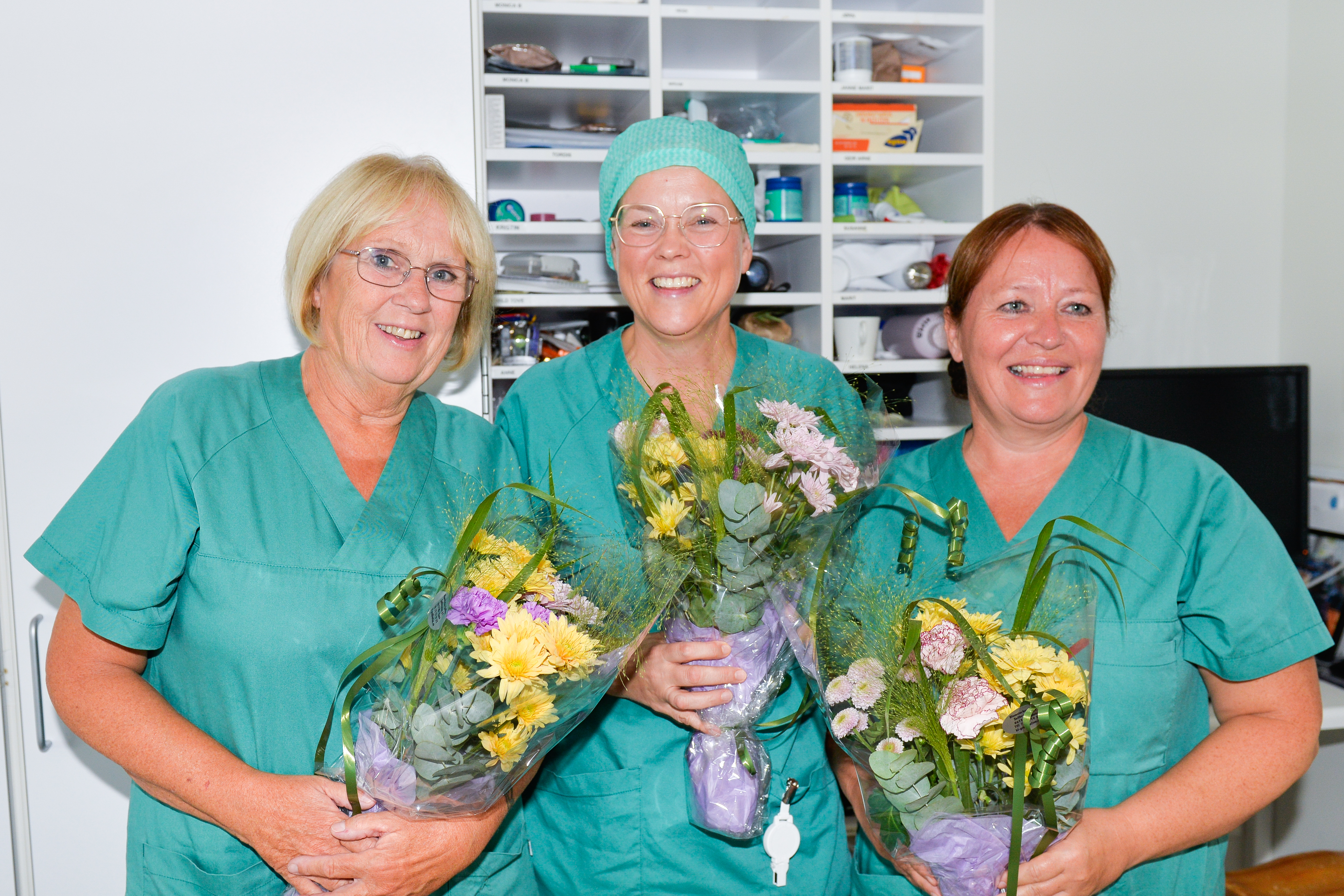 Tre damer smiler og holder hver sin blomsterbukett