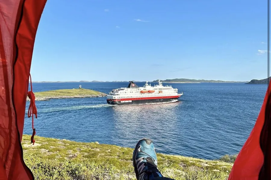 Hurtigruta glir forbi mens en person ligger i et telt med ene foten ut, og ser på