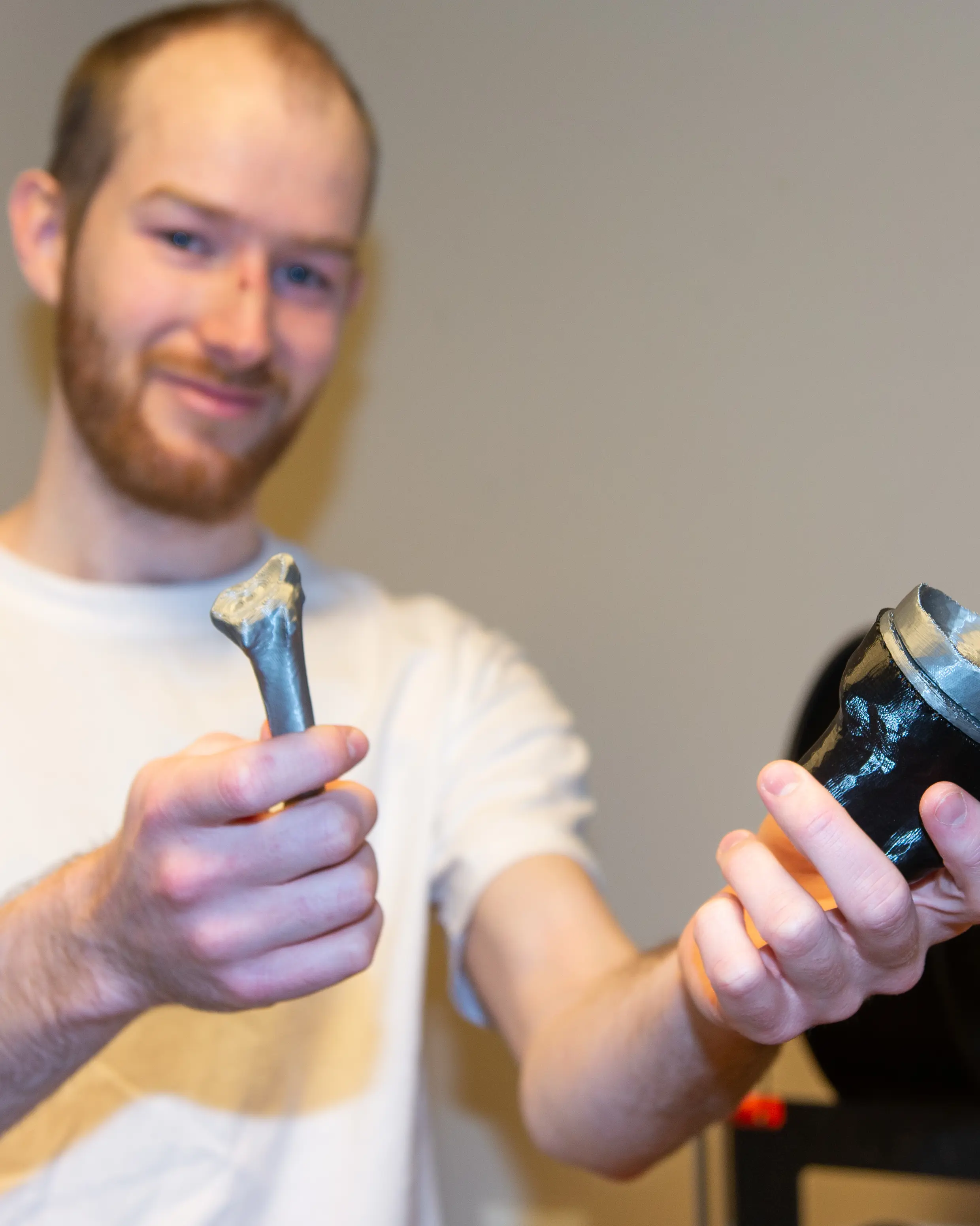 Ung mann i hvit T-skljorte som holder et 3D-printet beinfragment