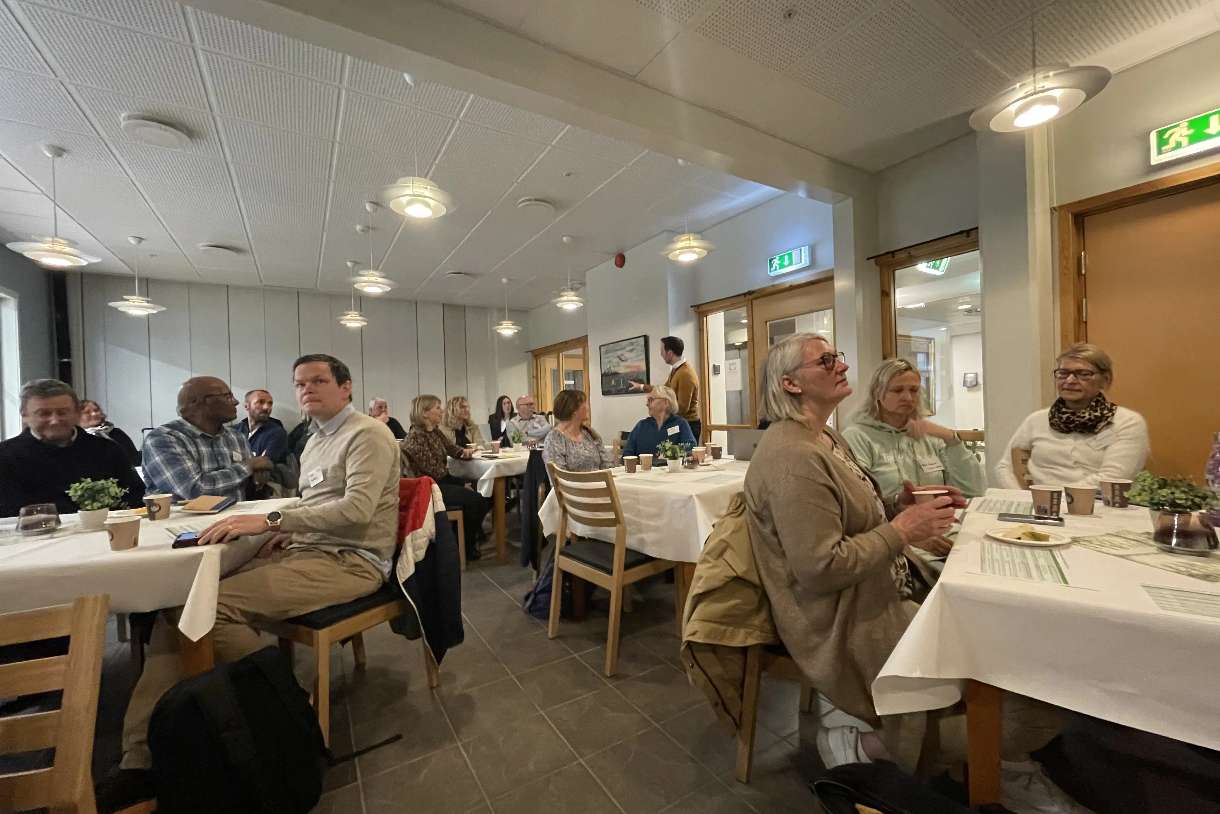 Mange mennesker i et lokale hører på en forelesning