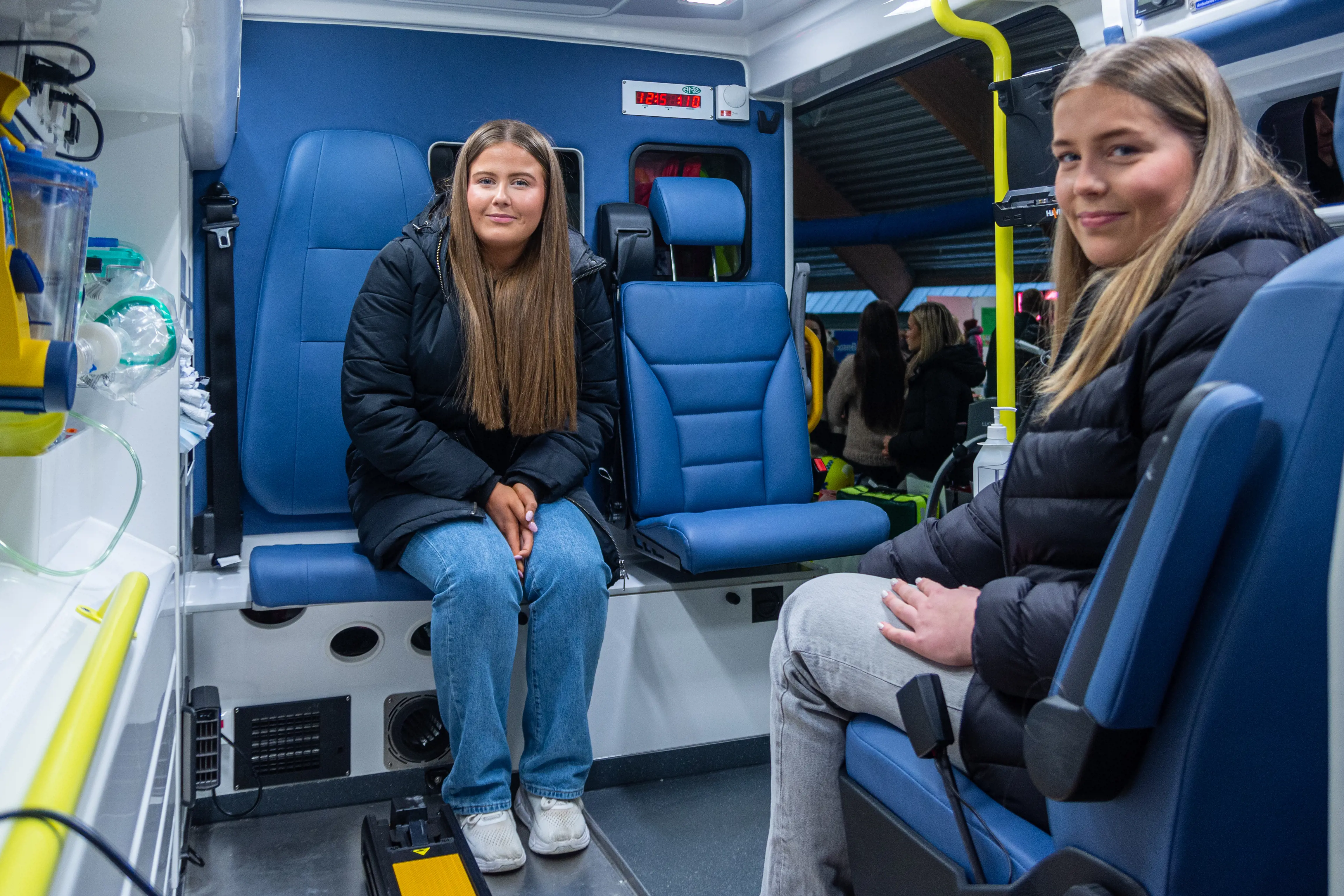 To unge damer sitter på hver sin stol i en ambulanse