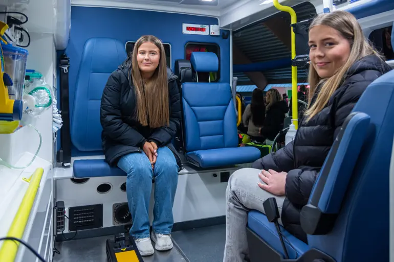 To unge damer sitter på hver sin stol i en ambulanse
