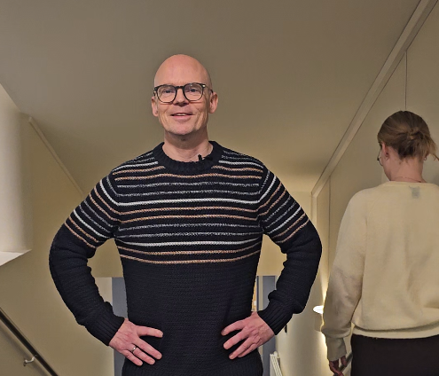 En mann med briller står med armene i siden og smiler til kamera