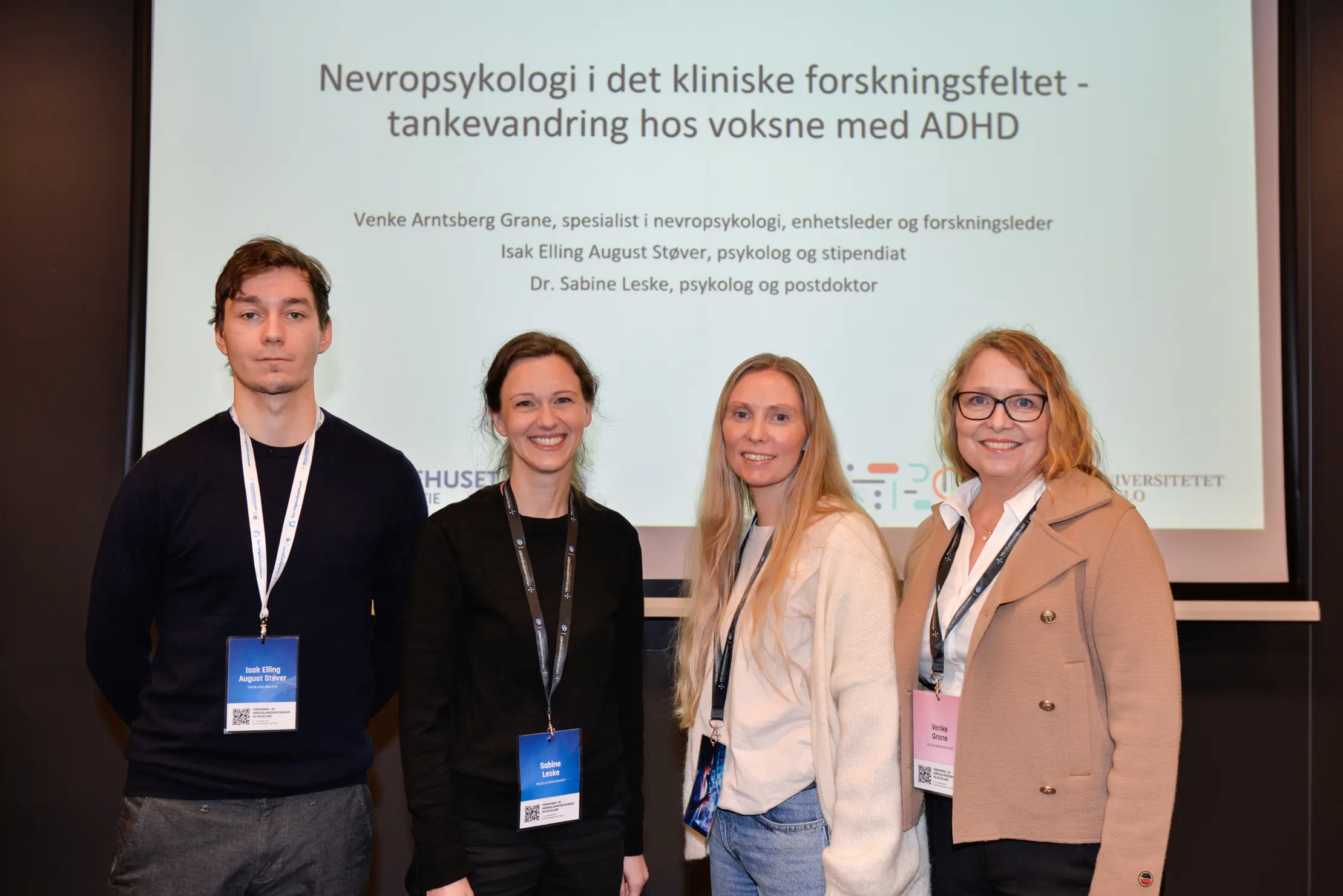 Tre kvinner og en mann står foran en stor skjerm med innhold om nevropsykologi