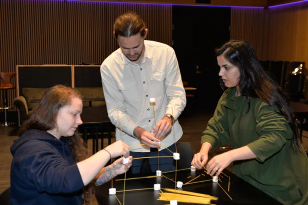Tre personer bygger tårn av spagetti og marshmallows
