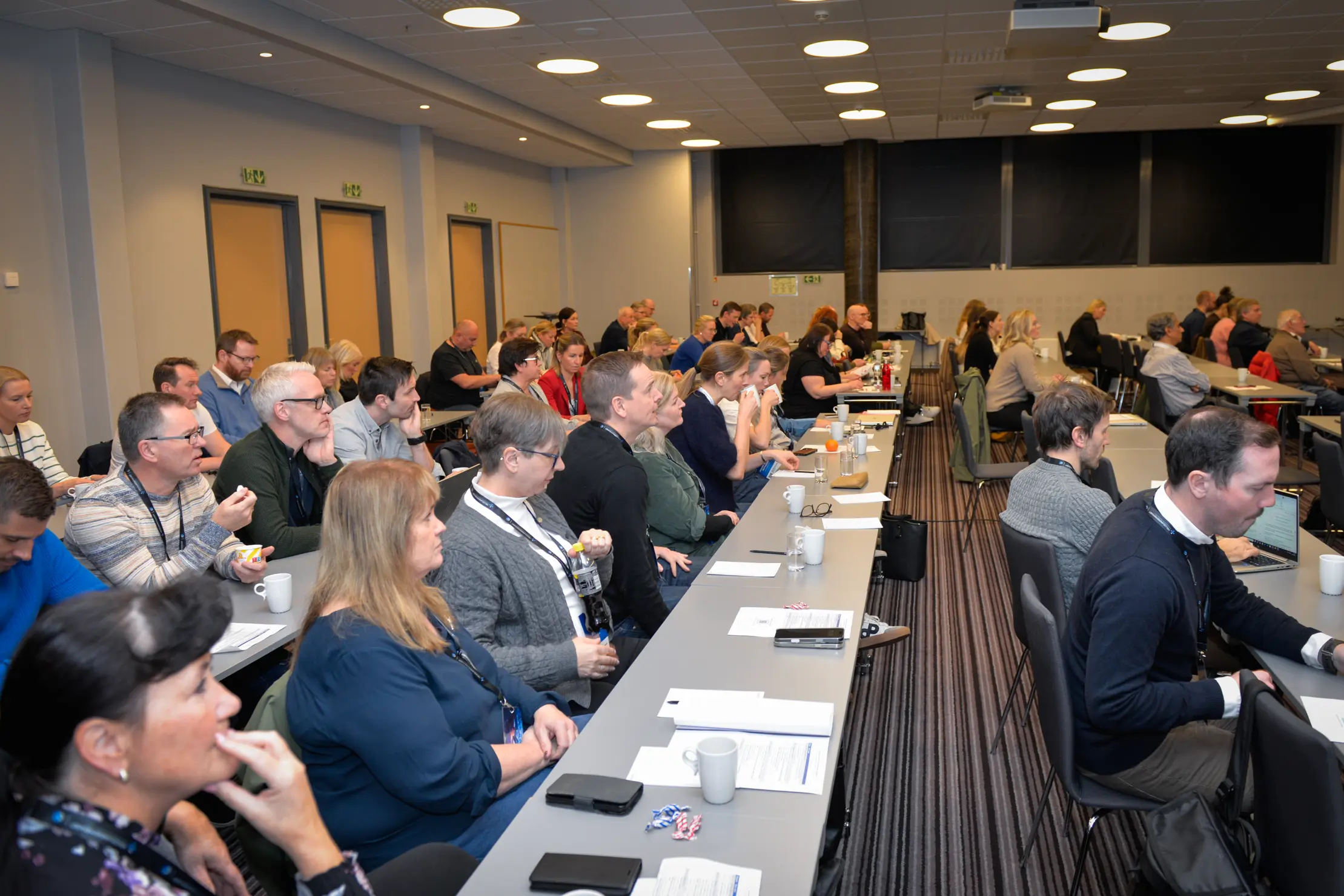 Et stort rom fullt av mennesker som sitter på rekke bak pulter