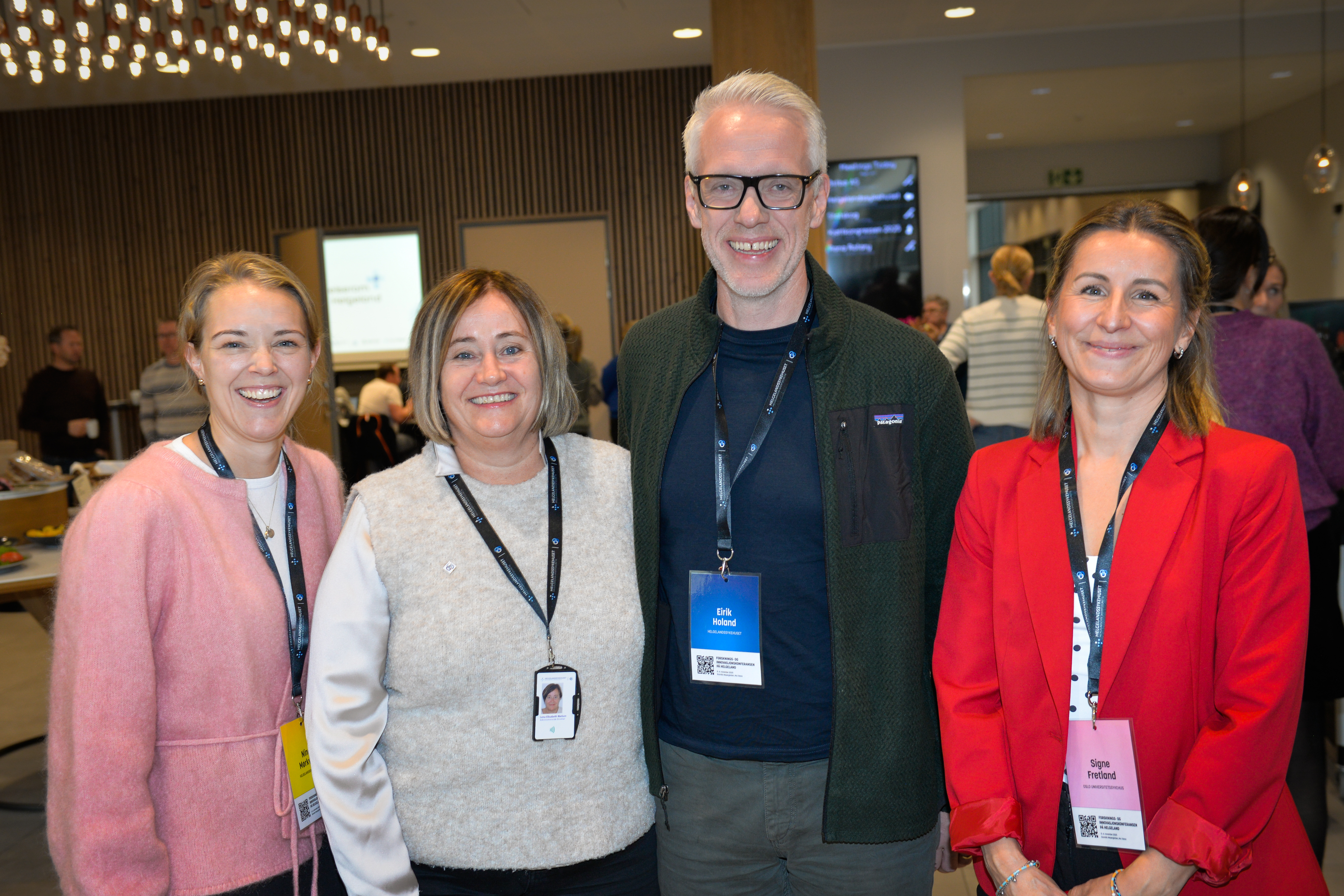 Tre kvinner og en mann ser inn i kameraet og smiler