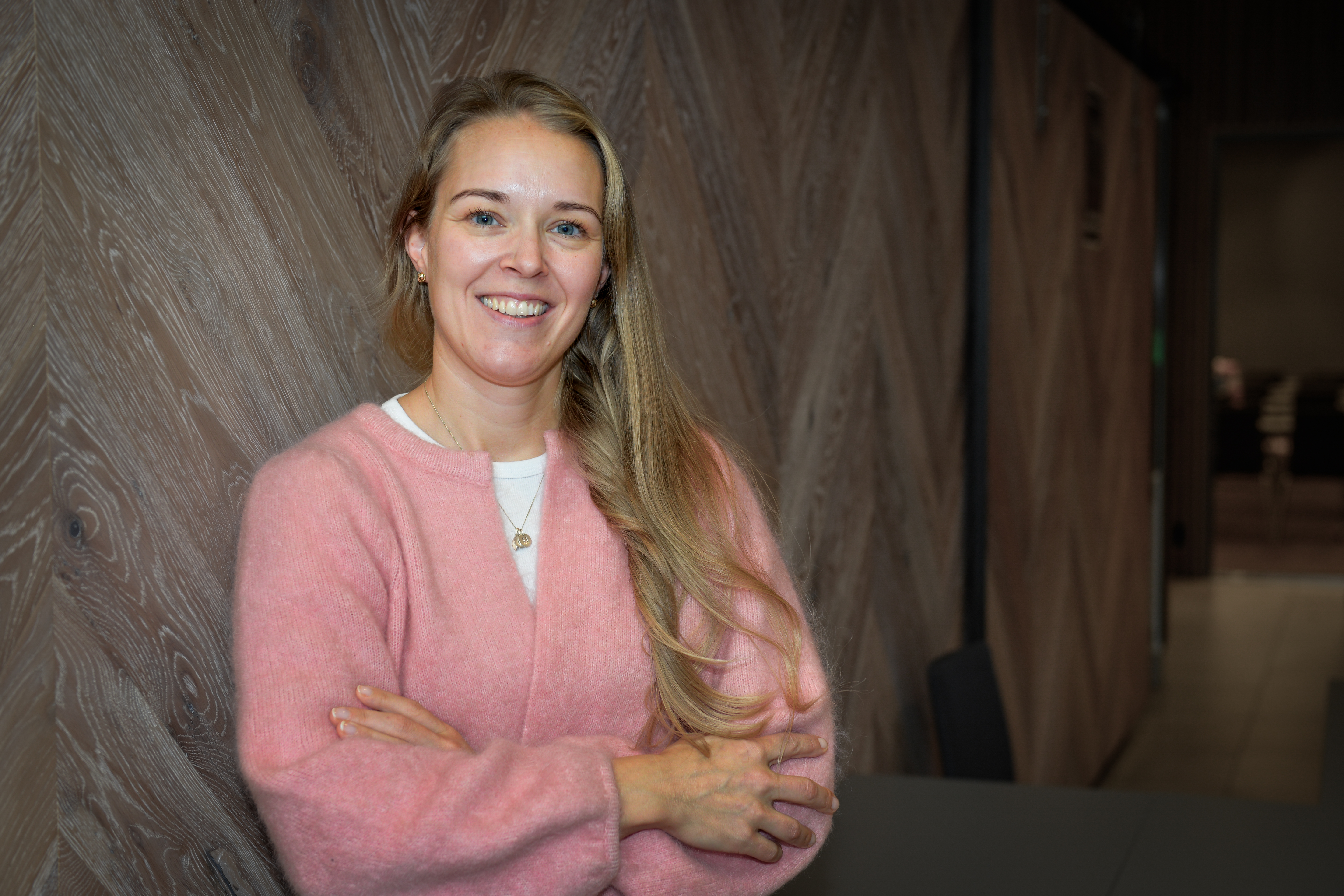 Smilende dame i rosa genser lener seg mot en vegg