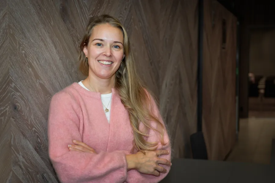 Smilende dame i rosa genser lener seg mot en vegg