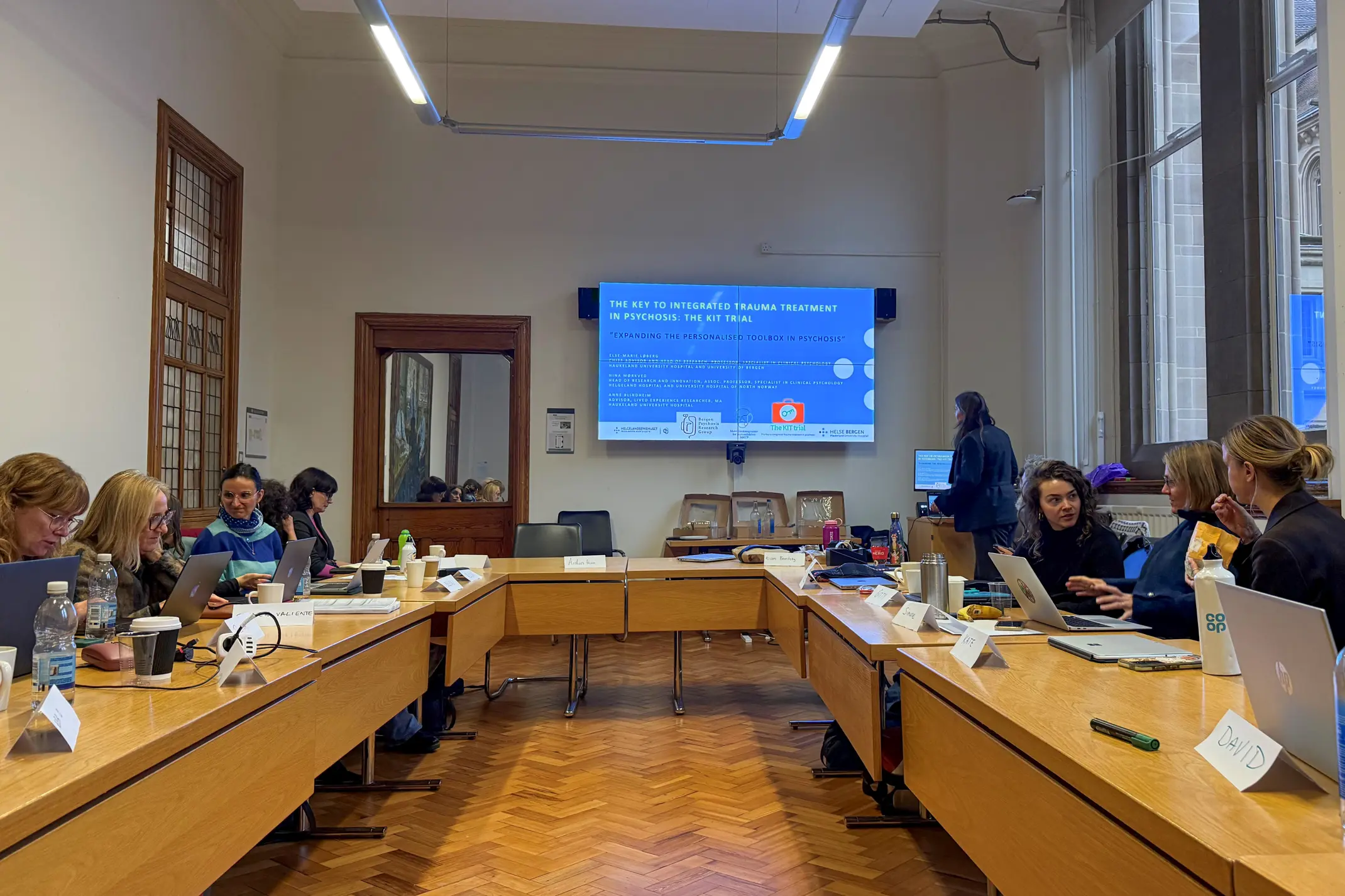 Flere mennesker sitter langs bord på begge sider av bordet og snakker med hverandre